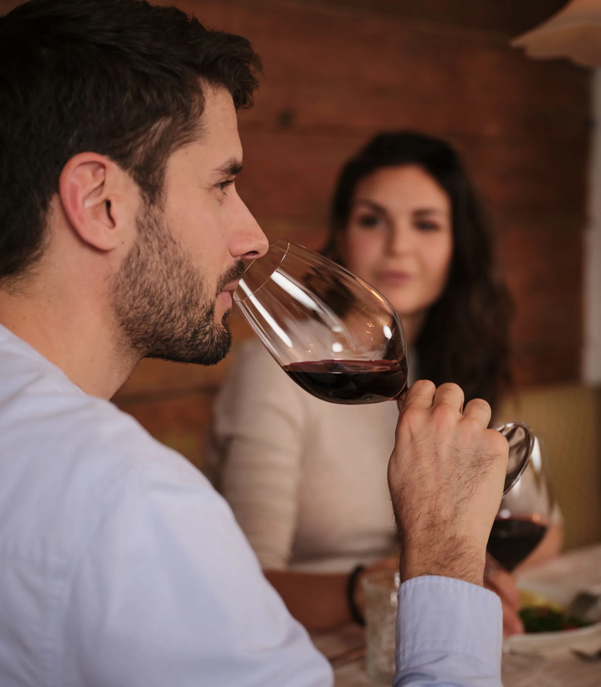 Mann trinkt Rotwein, Frau im Hintergrund unscharf