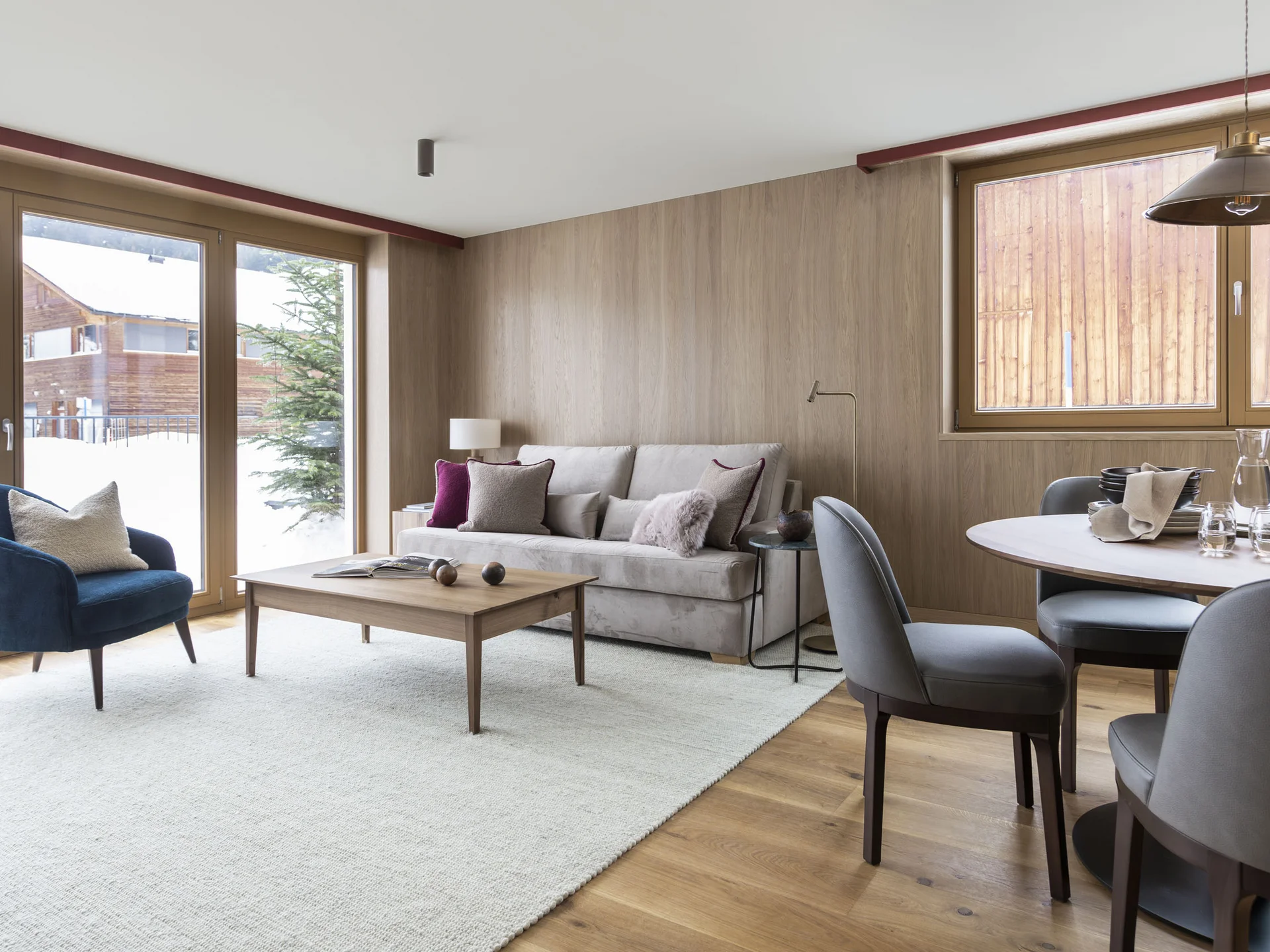 Gemütliches Wohnzimmer mit Sofa, Sesseln, Esstisch und großen Fenstern mit Bergblick