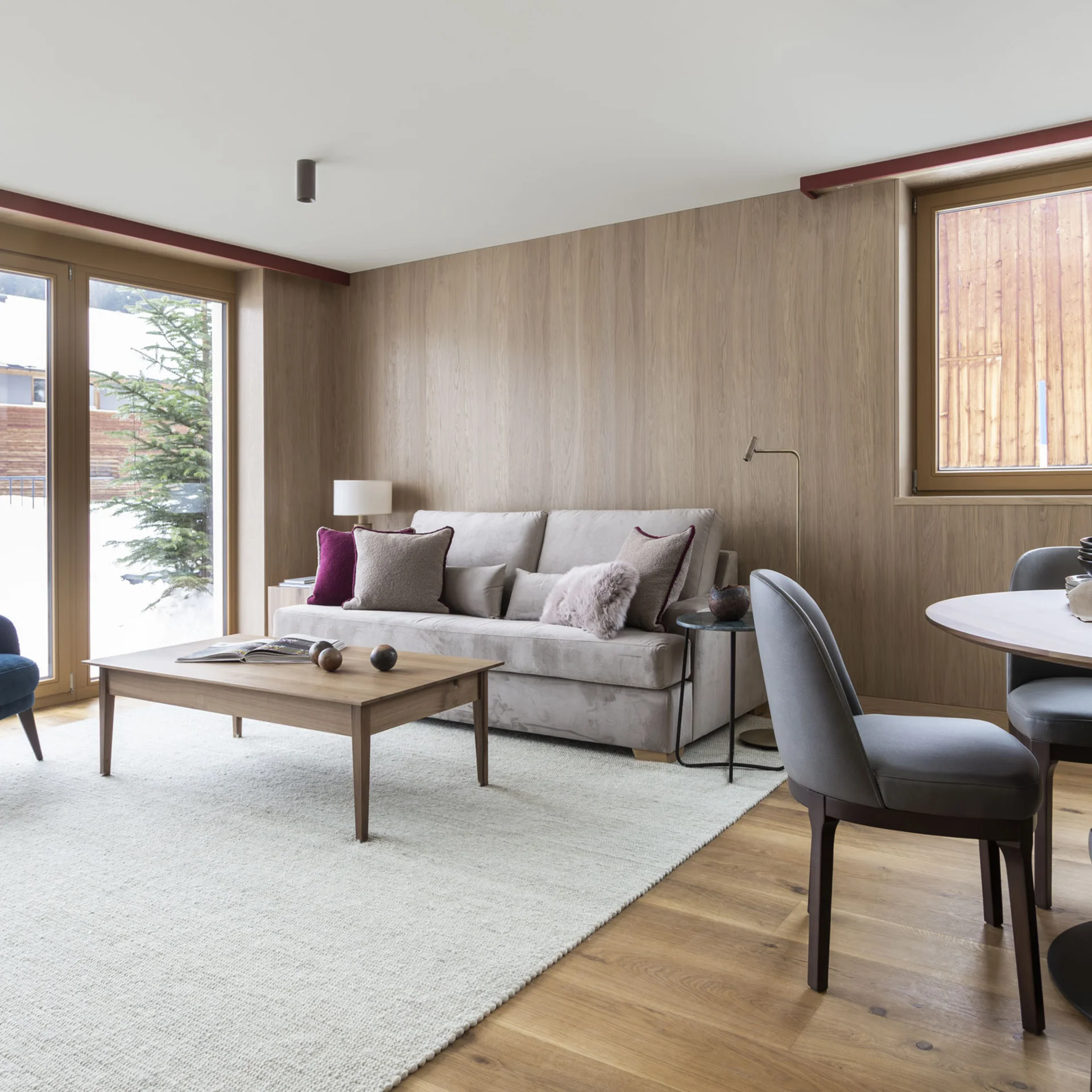 Gemütliches Wohnzimmer mit Sofa, Sesseln, Esstisch und großen Fenstern mit Bergblick