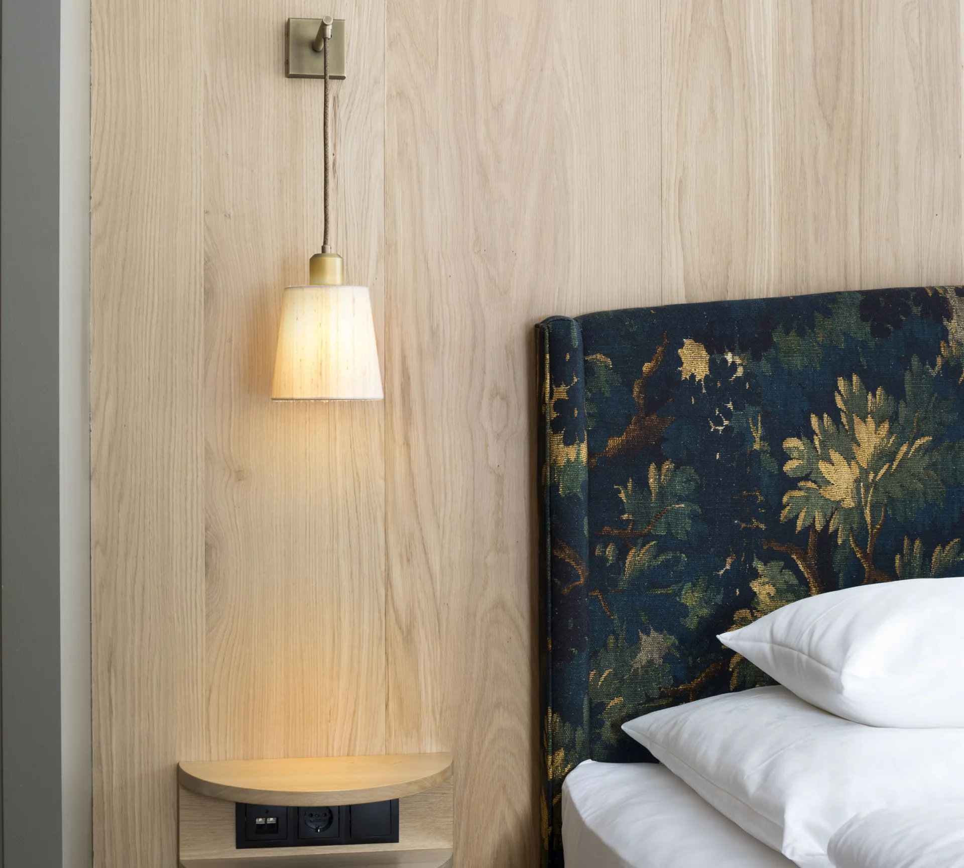 Wandlampe neben floral bezogenem Kopfteil und weißen Kissen