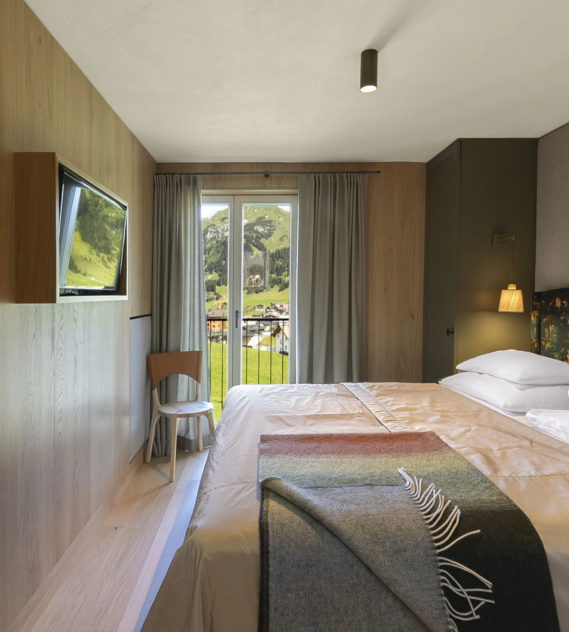 Modernes Hotelzimmer mit Doppelbett, Holzverkleidung und Balkon mit Blick auf Berge