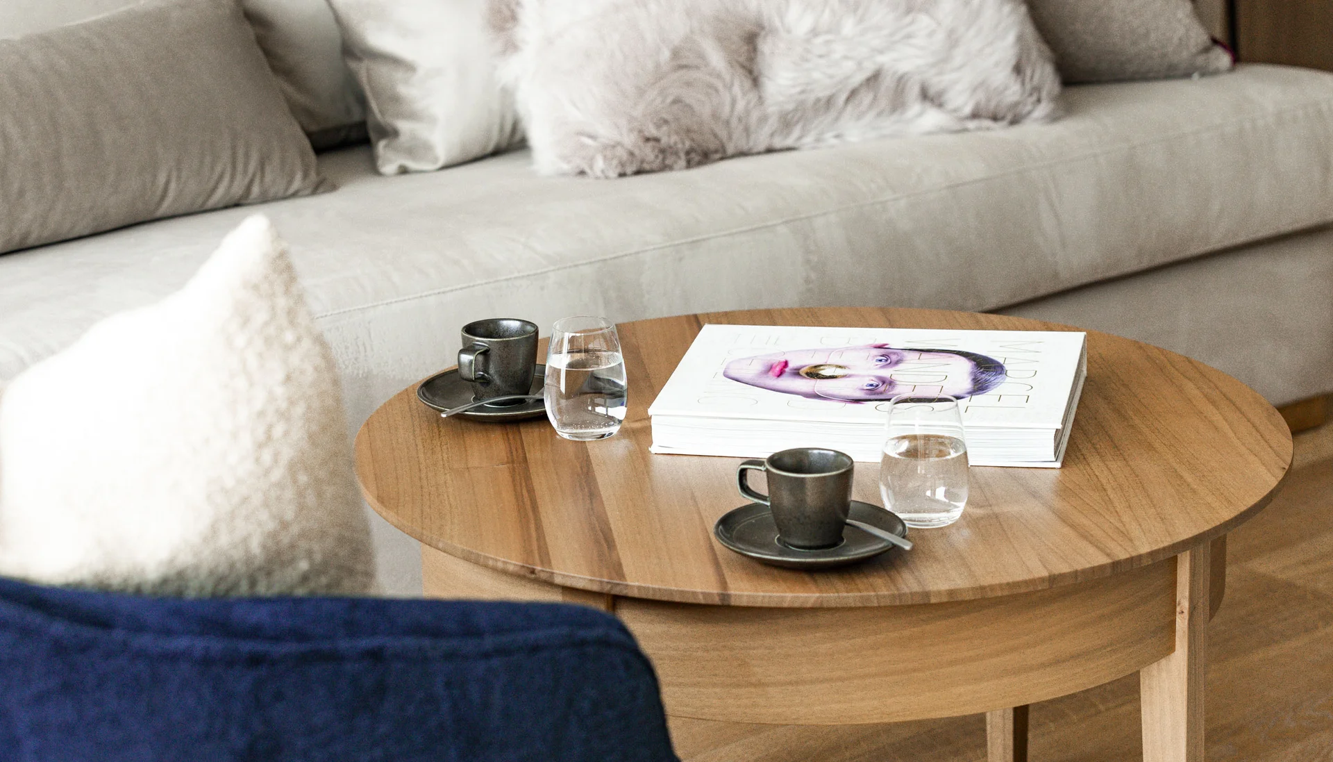 Wohnzimmer mit beigem Sofa, flauschigen Kissen und Holz-Couchtisch mit Tassen