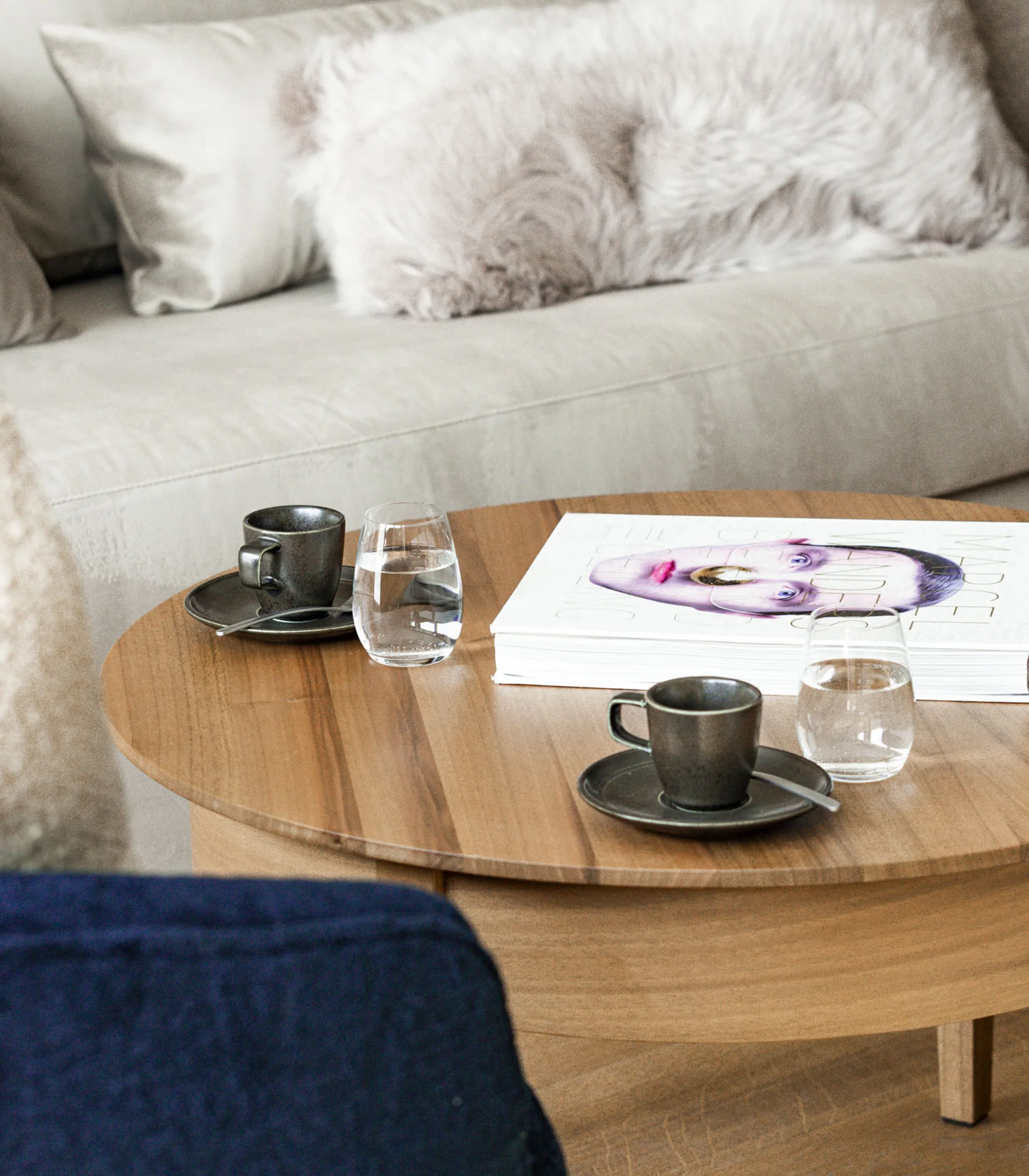 Wohnzimmer mit beigem Sofa, flauschigen Kissen und Holz-Couchtisch mit Tassen