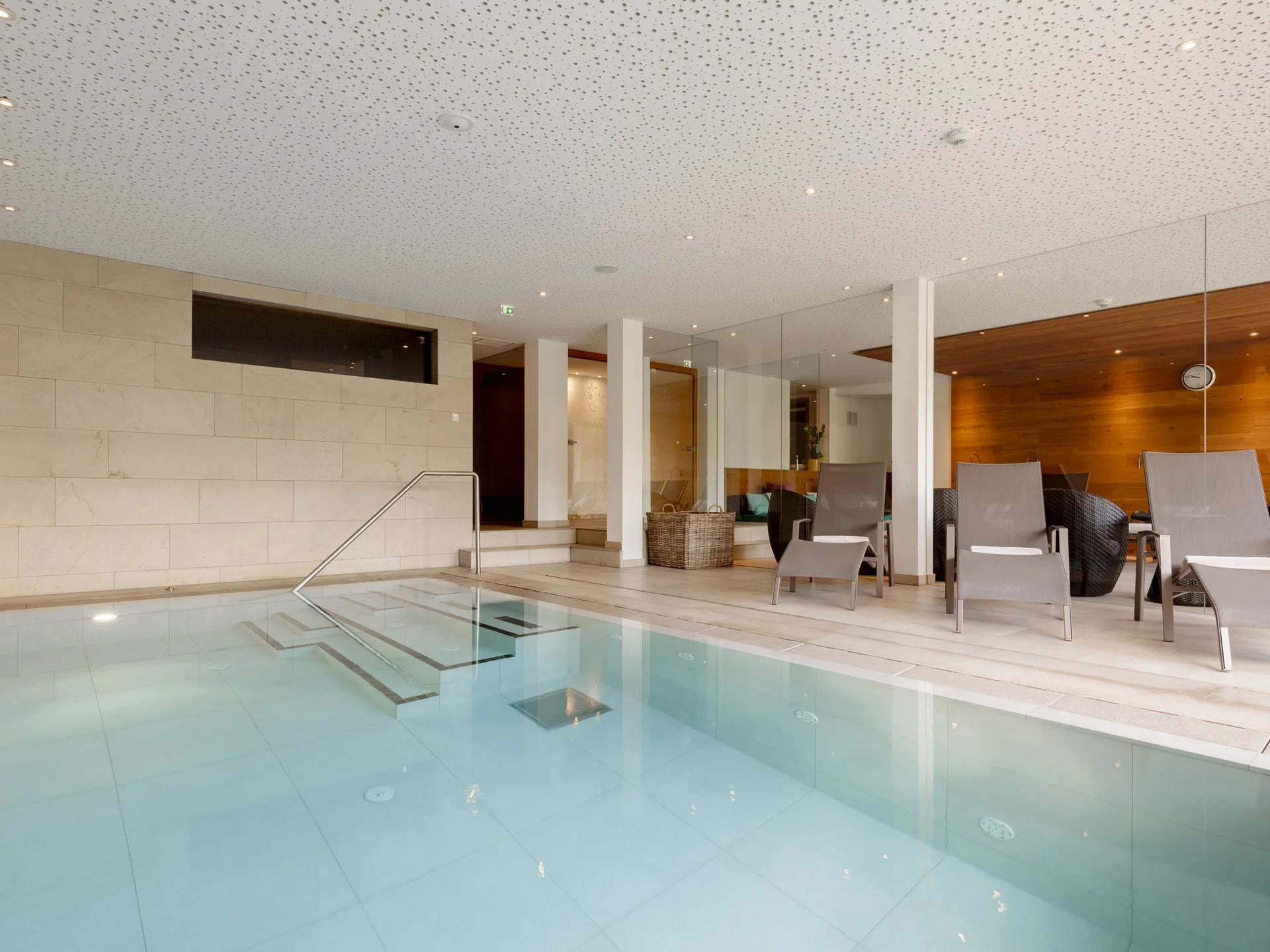 Moderner Innenpool mit Liegestühlen und Glaswand im Entspannungsraum