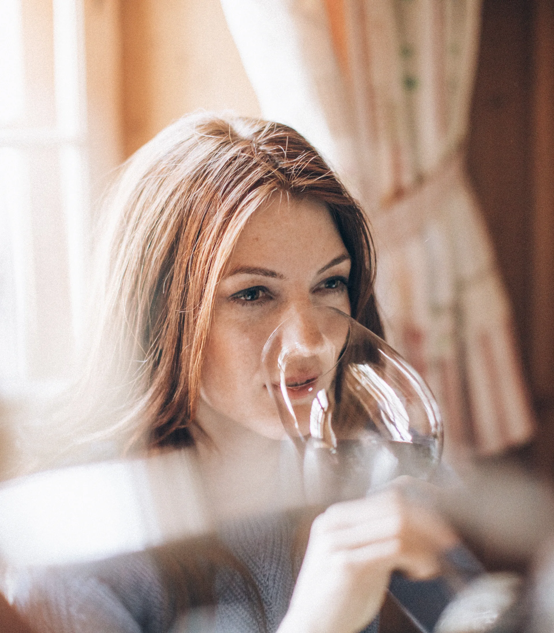 Frau trinkt aus einem Weinglas in einem gemütlichen Raum