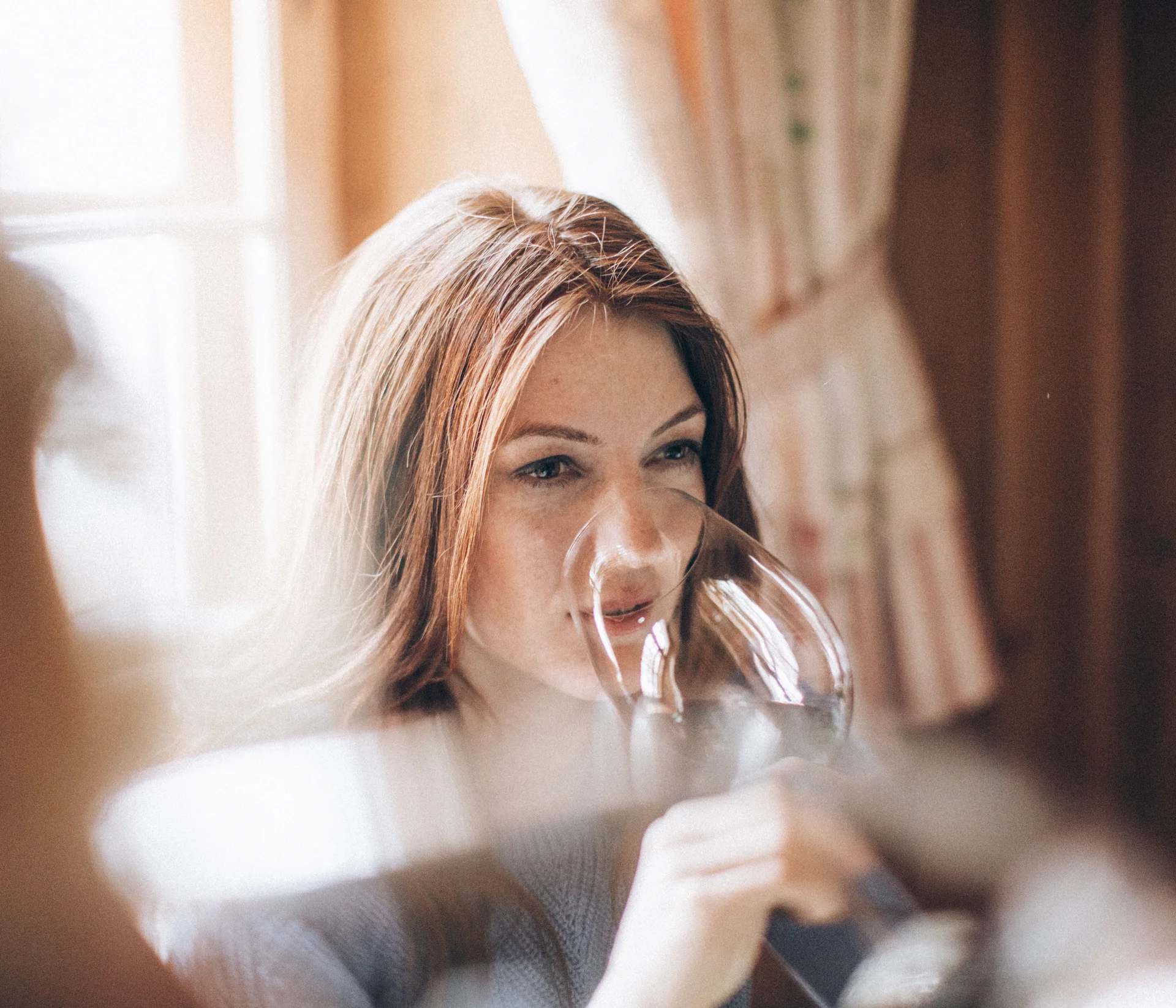 Frau trinkt aus einem Weinglas in einem gemütlichen Raum