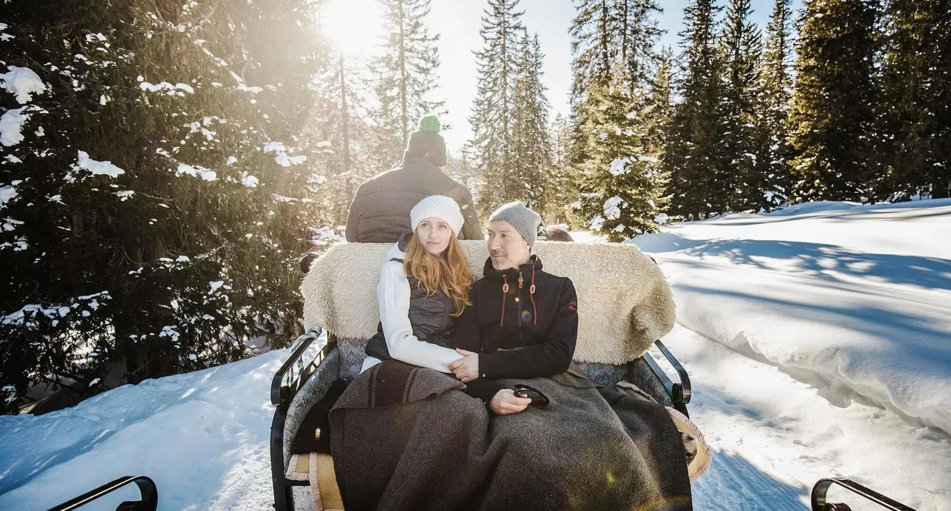 Paar sitzt auf Pferdeschlitten bei sonnigem Wintertag im Schnee