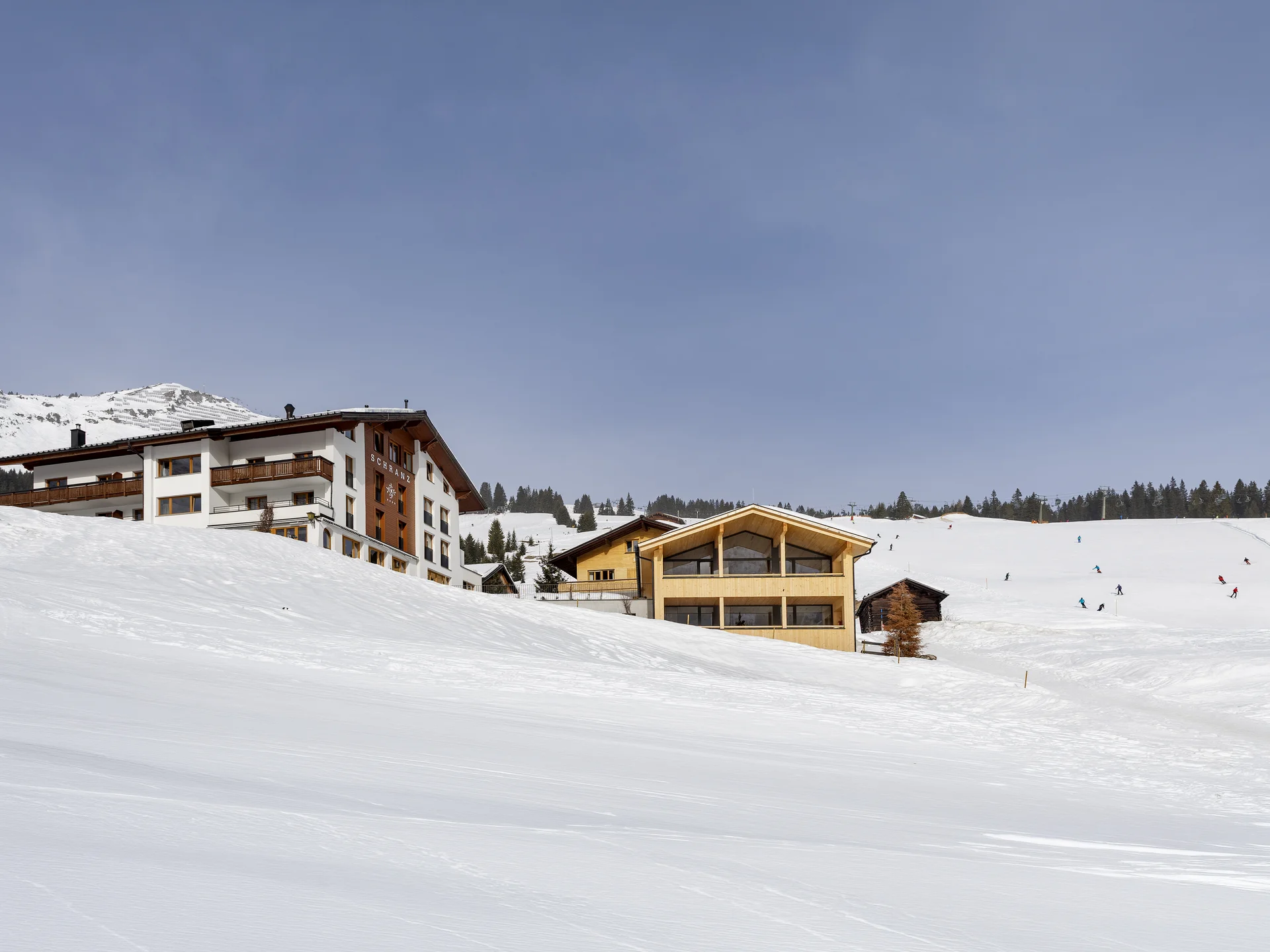 Bilder und Impressionen aus dem Sunora Schneebedeckte Häuser am Berghang mit Skifahrern im Skigebiet