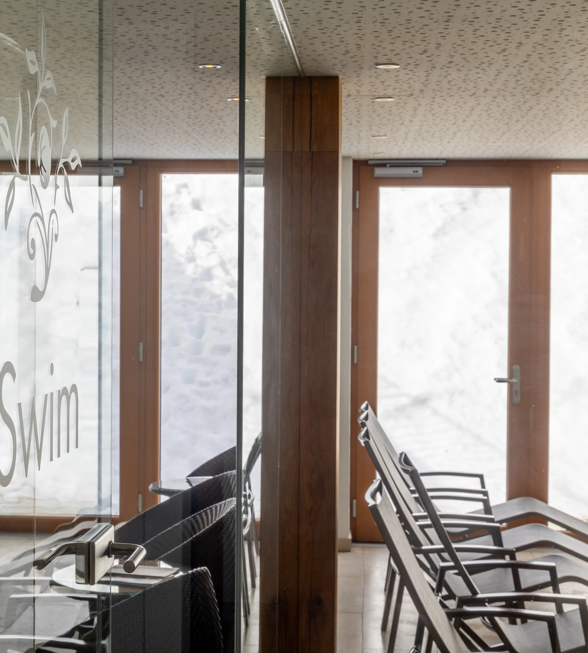 Ruhebereich mit Liegestühlen und Glasscheibe im Schwimmbad