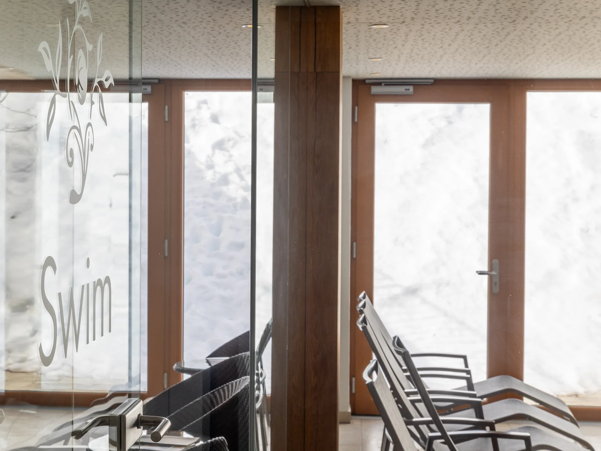 Ruhebereich mit Liegestühlen und Glasscheibe im Schwimmbad