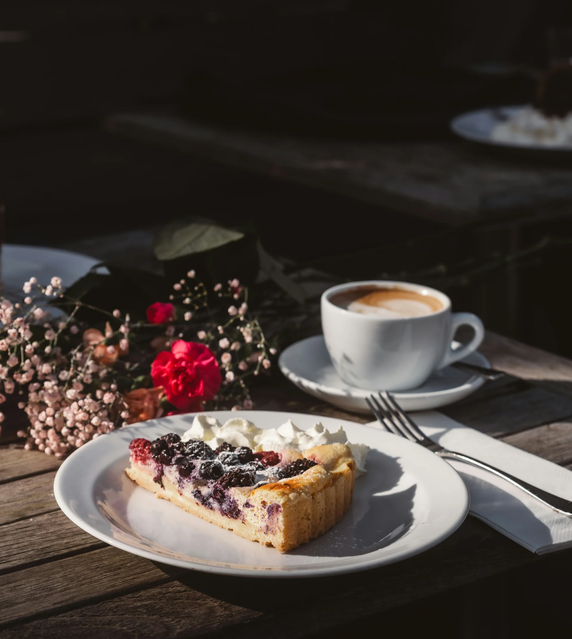 Kaffeetassen, Obstkuchen und Blumen auf einem Holztisch im Sonnenlicht