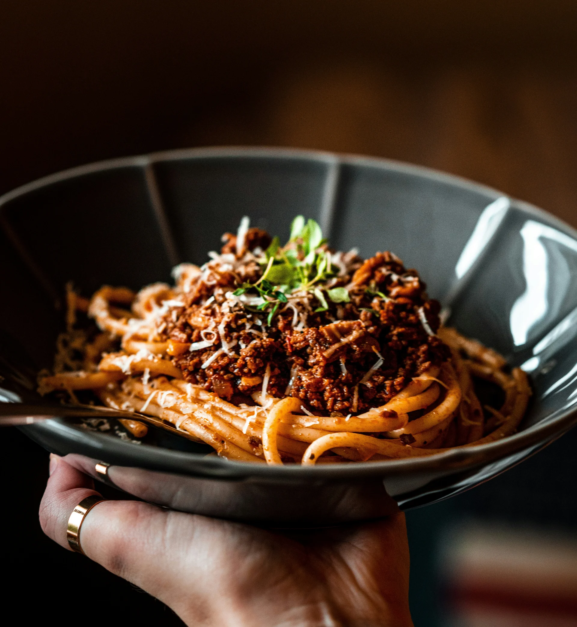 Hand holding black plate with spaghetti Bolognese topped with herbs