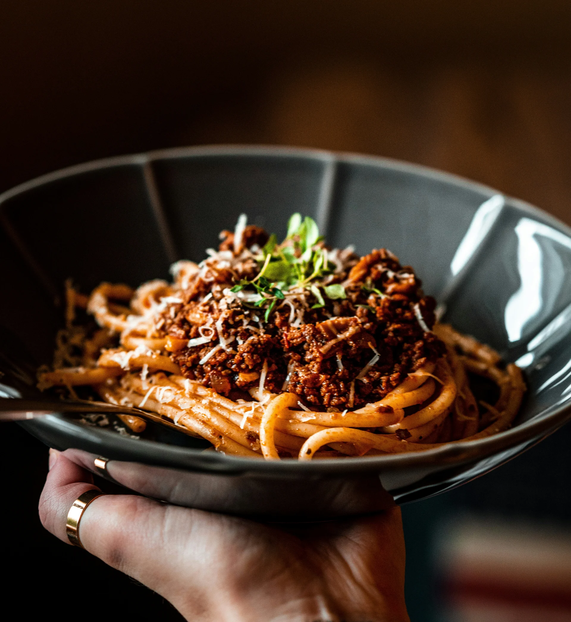 Hand hält schwarzen Teller mit Spaghetti Bolognese und Kräutern