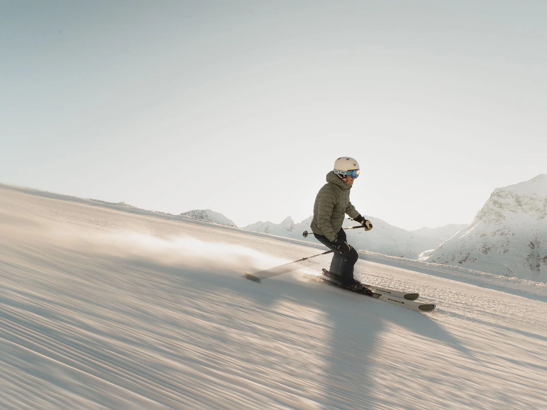 Skifahrer fährt bei klarem Himmel auf präparierter Piste in den Bergen
