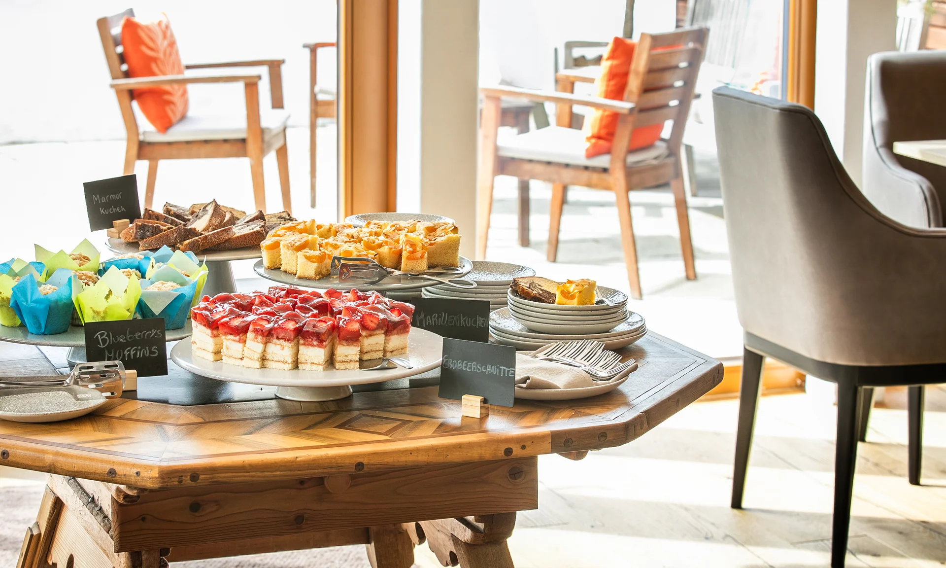 Tisch mit verschiedenen Kuchen und Muffins in einem hellen Raum mit Stühlen