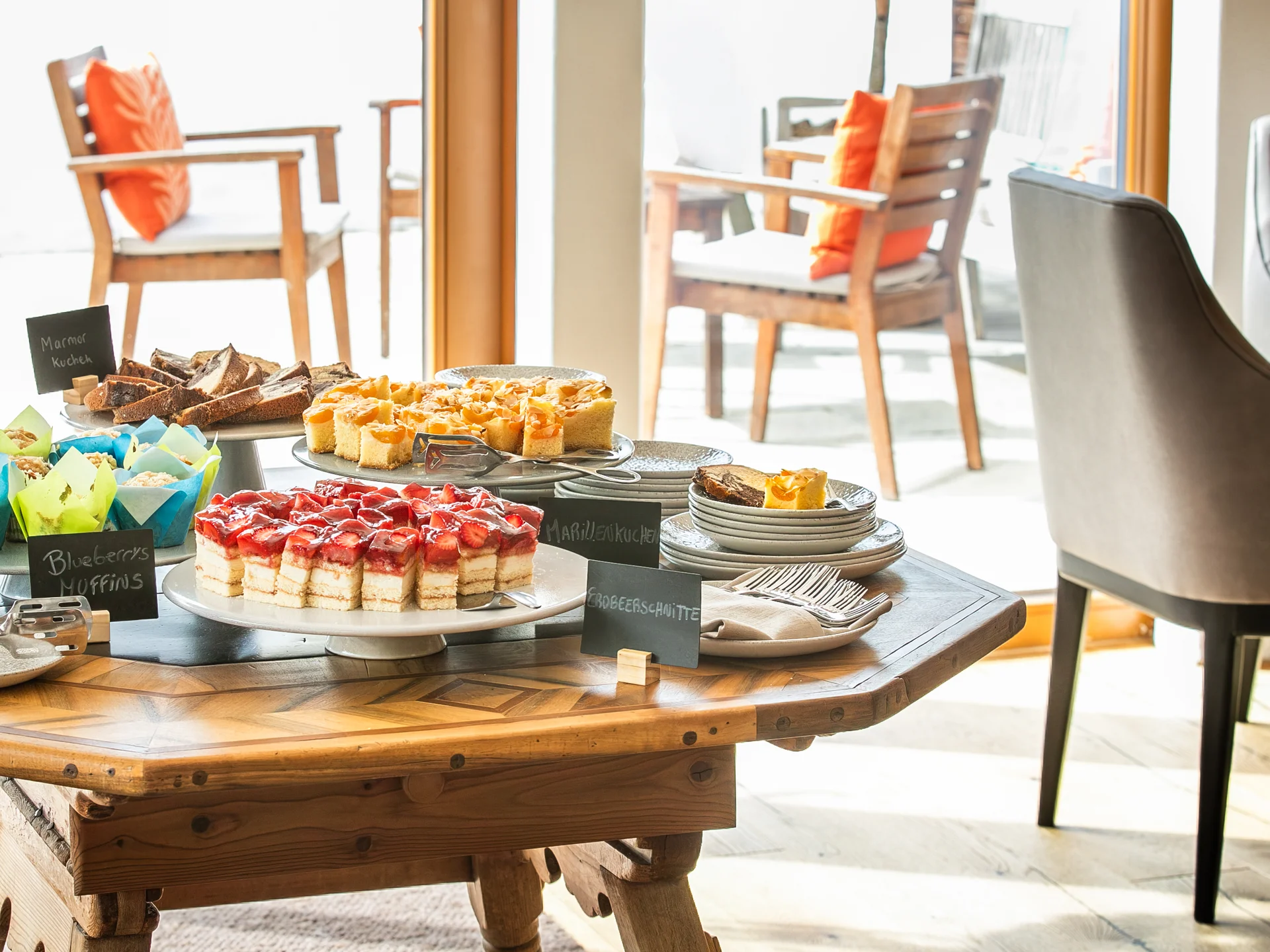 Bilder und Impressionen aus dem Sunora Tisch mit verschiedenen Kuchen und Muffins in einem hellen Raum mit Stühlen