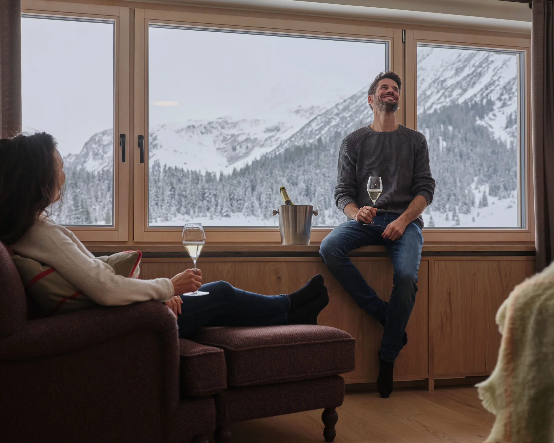 Mann und Frau genießen Wein vor Fenster mit Schneebergen