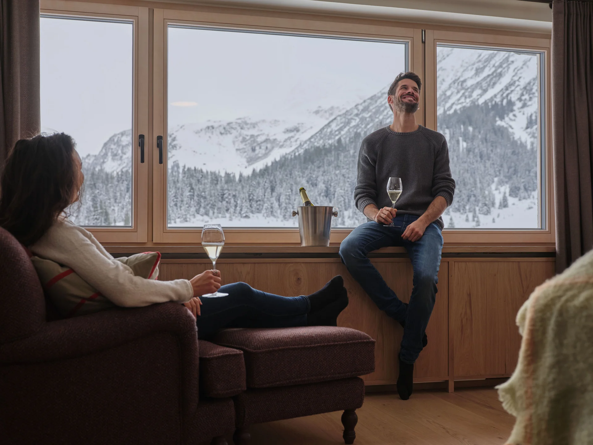 Mann und Frau genießen Wein vor Fenster mit Schneebergen