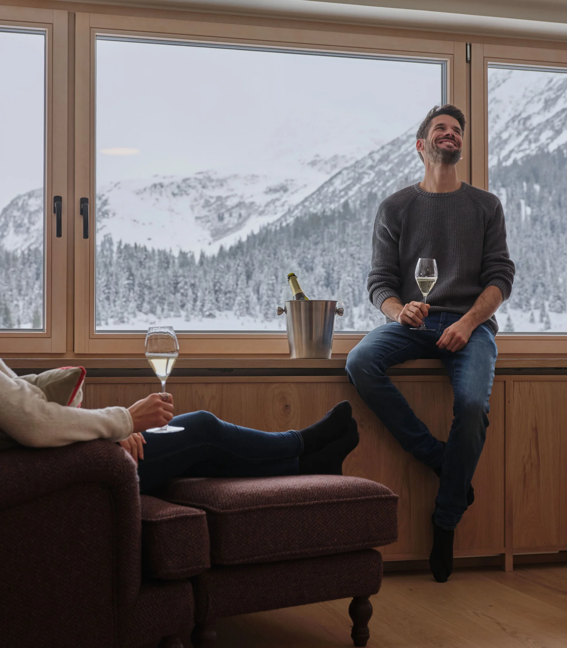 Mann und Frau genießen Wein vor Fenster mit Schneebergen