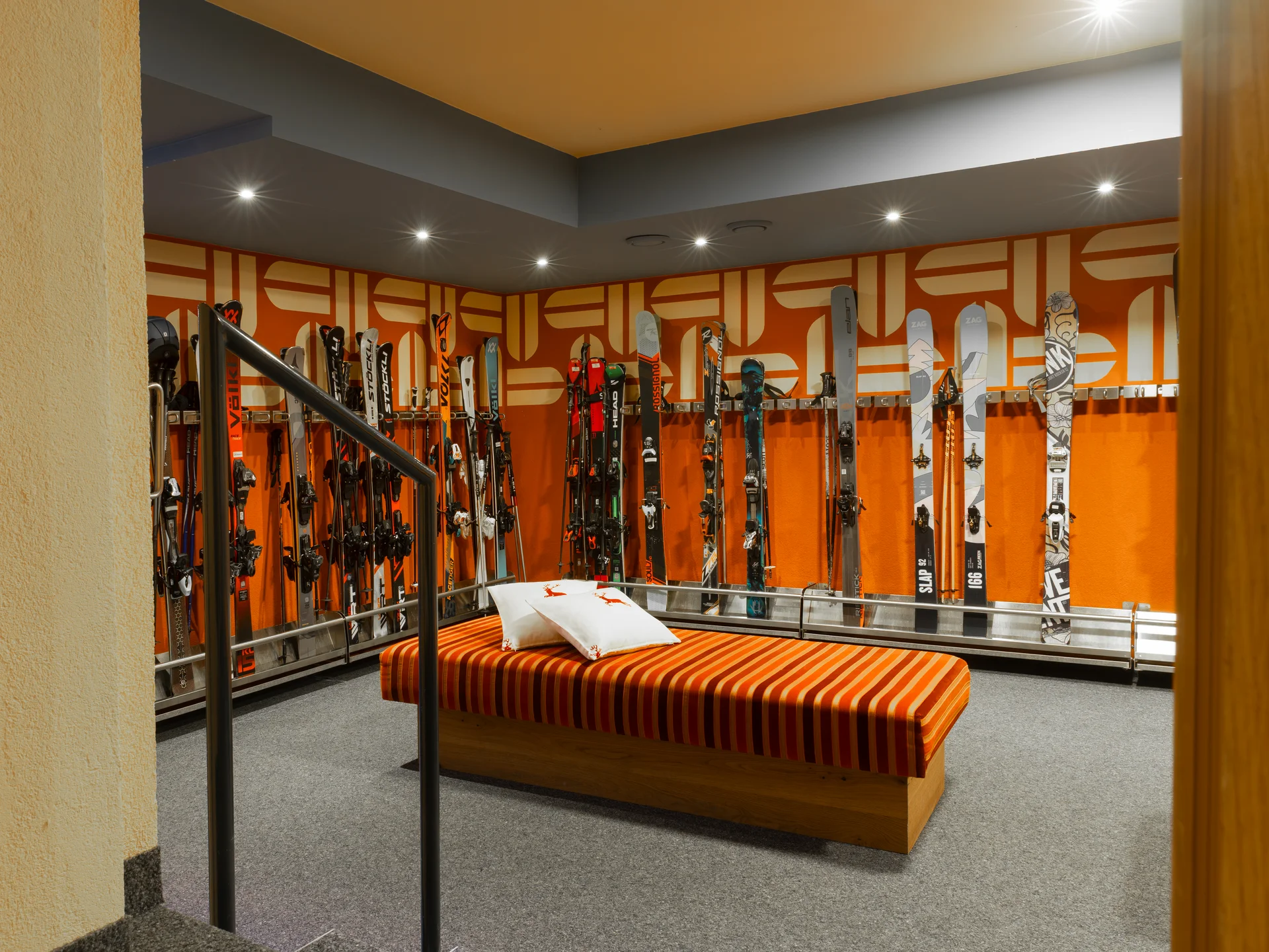Skiraum mit bunten Skiern und orange gestreifter Bank mit Kissen