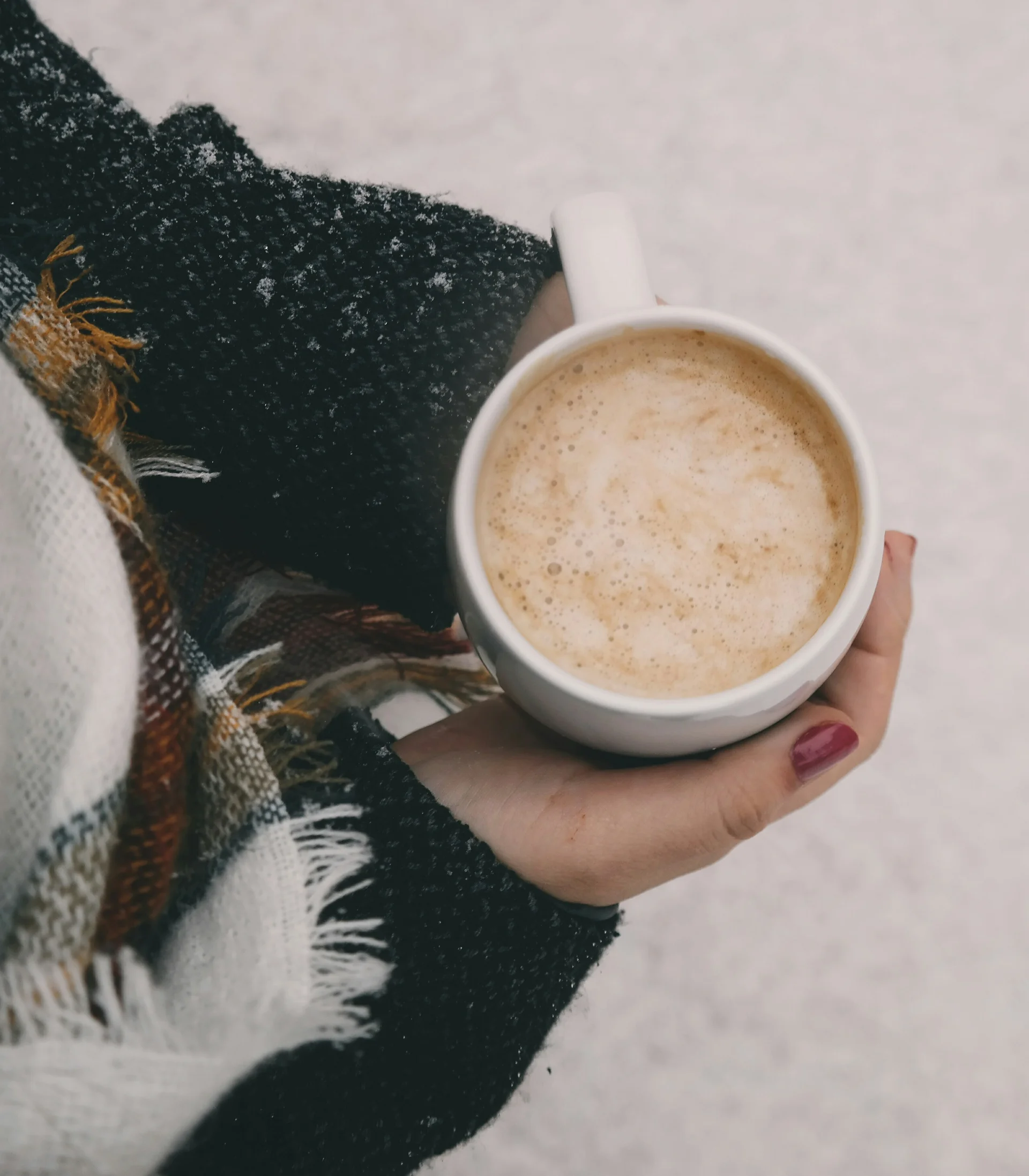 Nahaufnahme einer Hand, die eine Tasse Kaffee mit Schaum hält