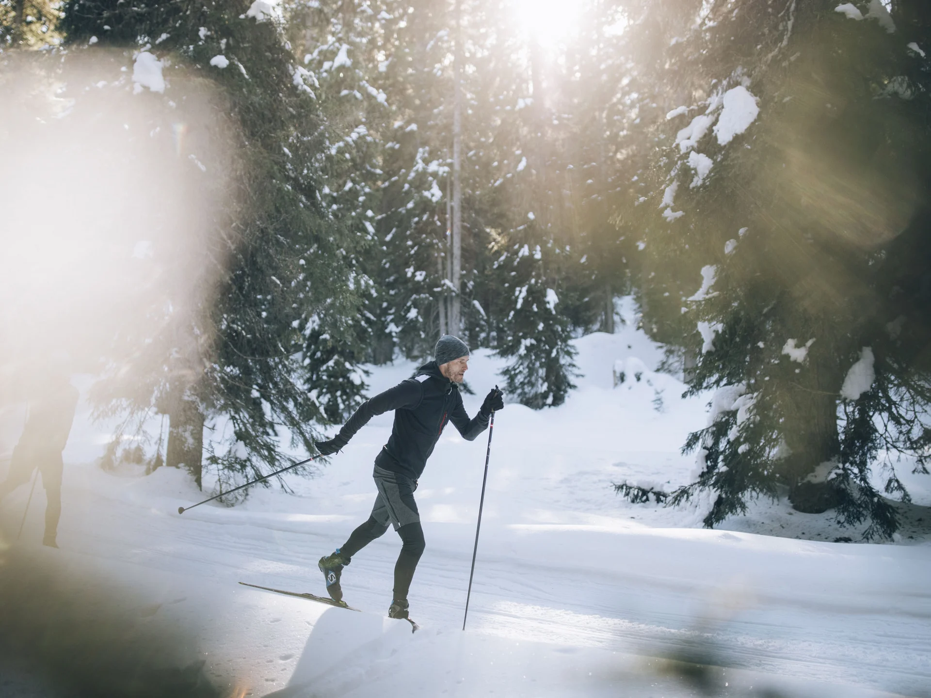 Mann beim Langlaufen auf verschneitem Waldweg bei Sonnenschein
