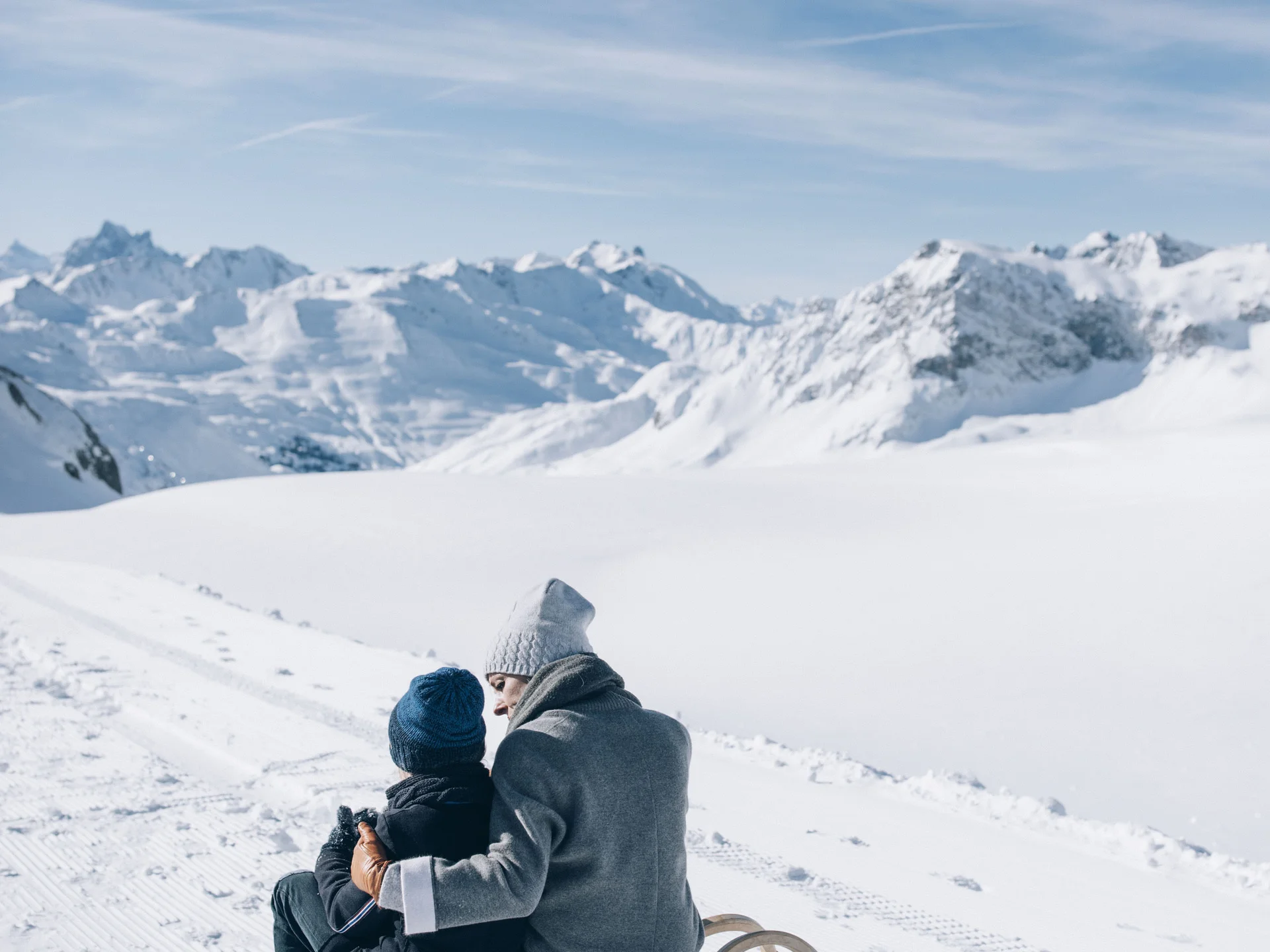 Personen auf Schlitten in verschneiter Berglandschaft bei klarem Himmel