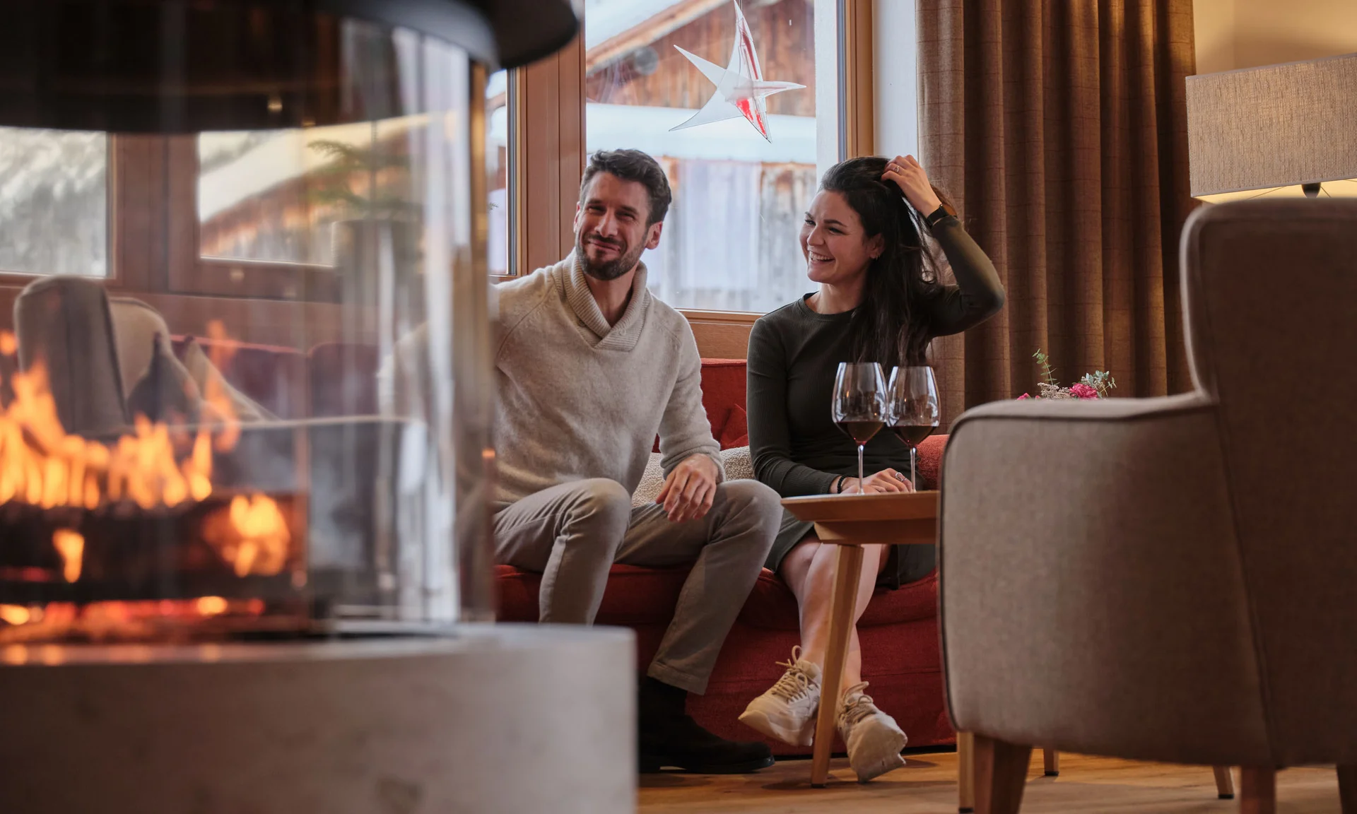 Paar sitzt gemütlich im Wohnzimmer am Kamin mit Weingläsern