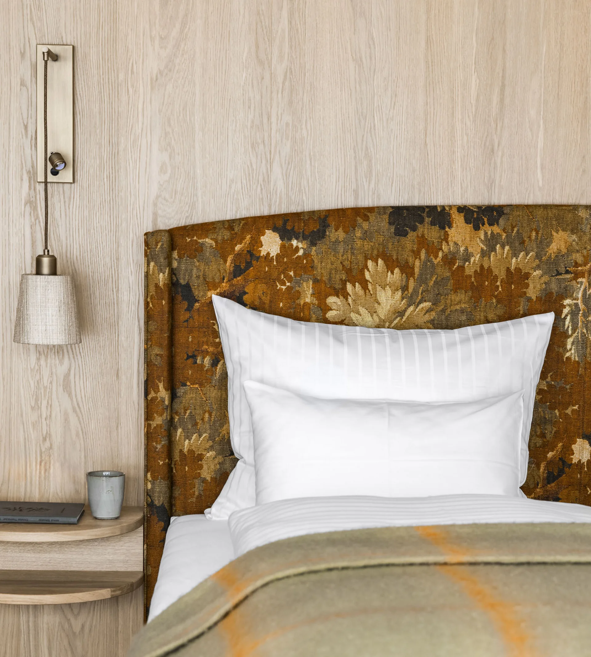 Nahaufnahme eines Bettes mit gemustertem Kopfteil und Nachttisch mit Lampe und Buch