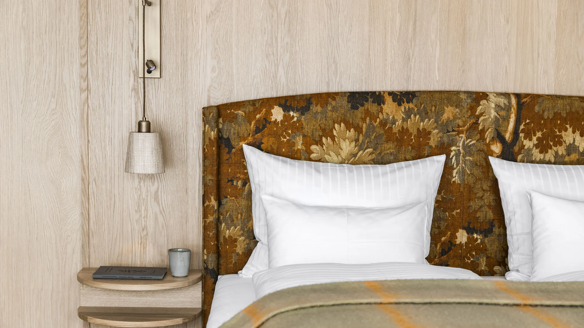 Nahaufnahme eines Bettes mit gemustertem Kopfteil und Nachttisch mit Lampe und Buch