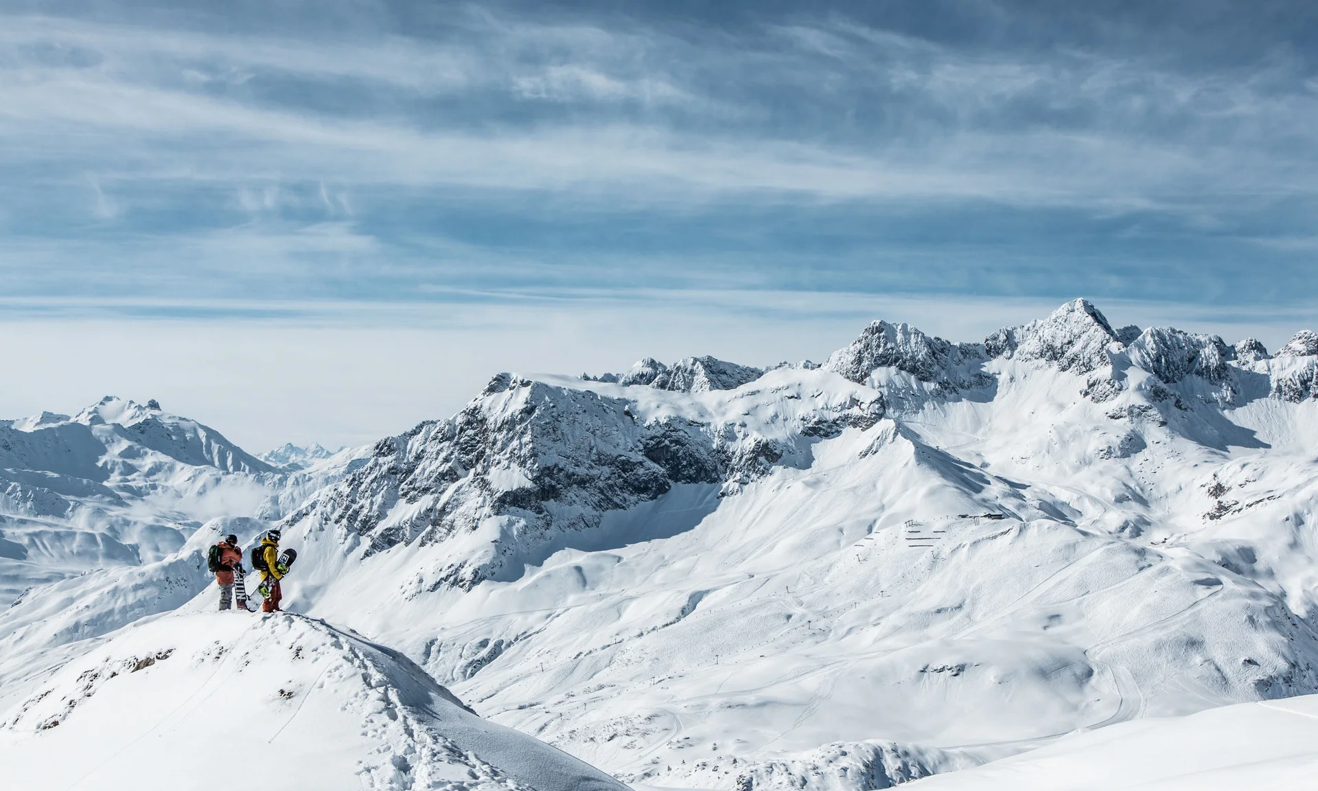 Zwei Snowboarder auf schneebedecktem Berg mit Alpen im Hintergrund