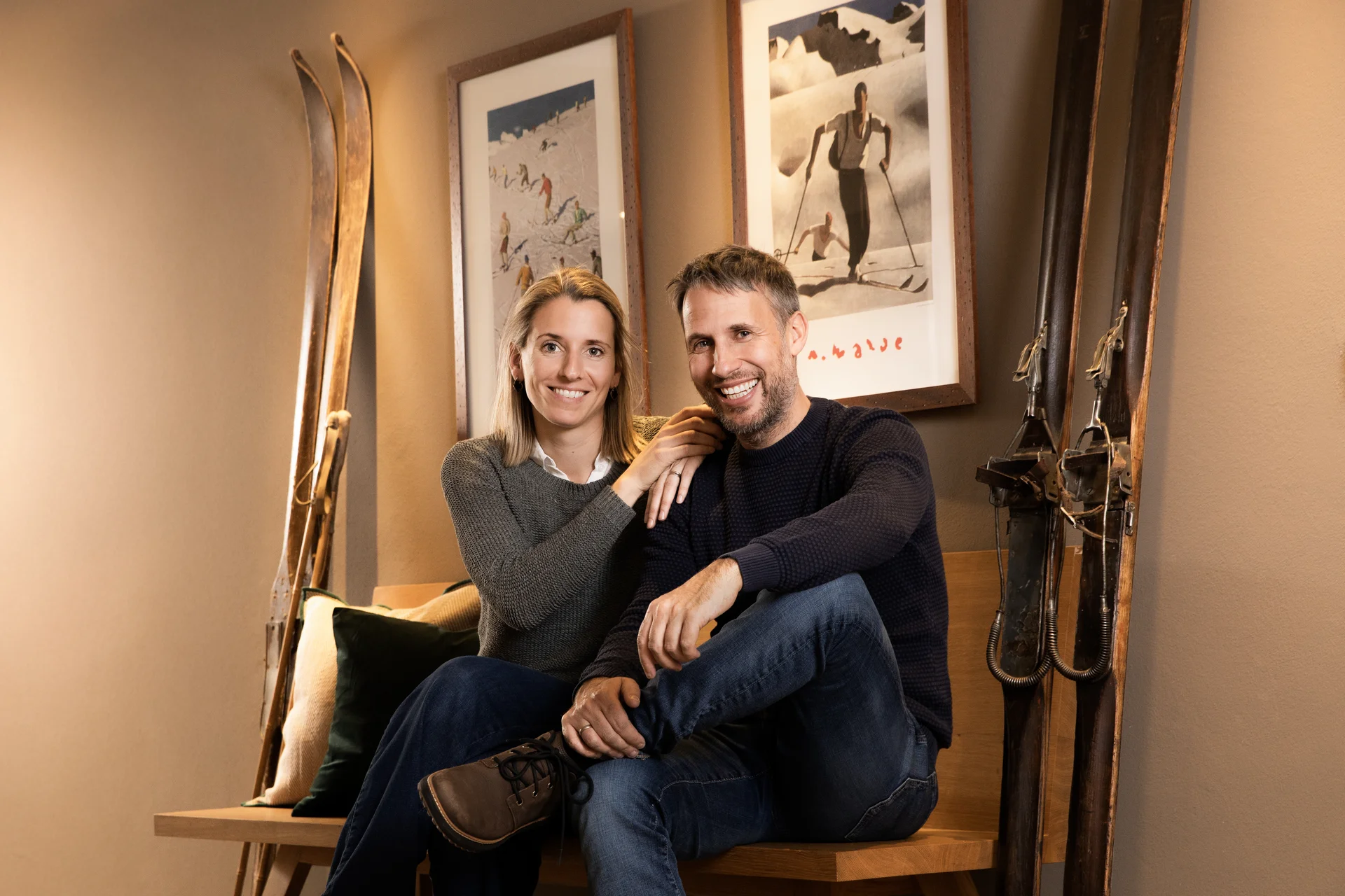 Lächelndes Paar sitzt auf einer Holzbank in einem Raum mit Skiern und Wintersportbildern