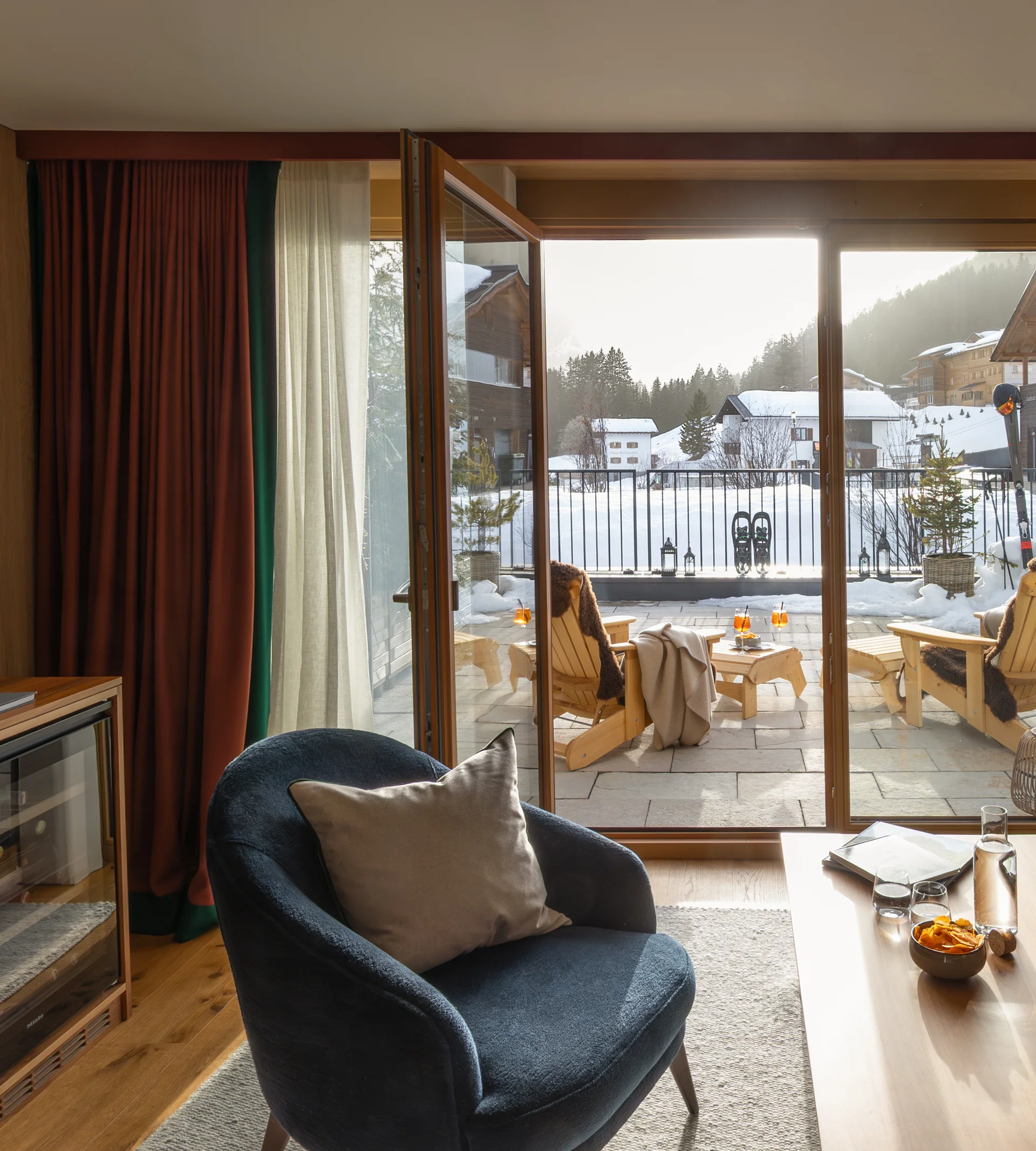 Gemütlicher Wohnbereich mit offenem Balkon und Blick auf verschneite Häuser und Berge