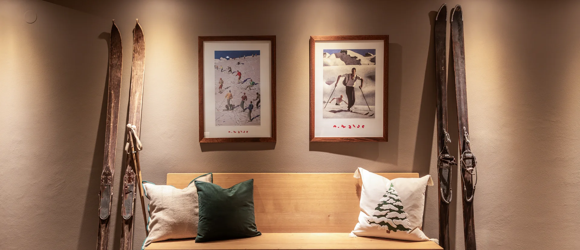 Holzbank mit Kissen unter zwei gerahmten Skifahrer-Bildern und antiken Skiern an der Wand