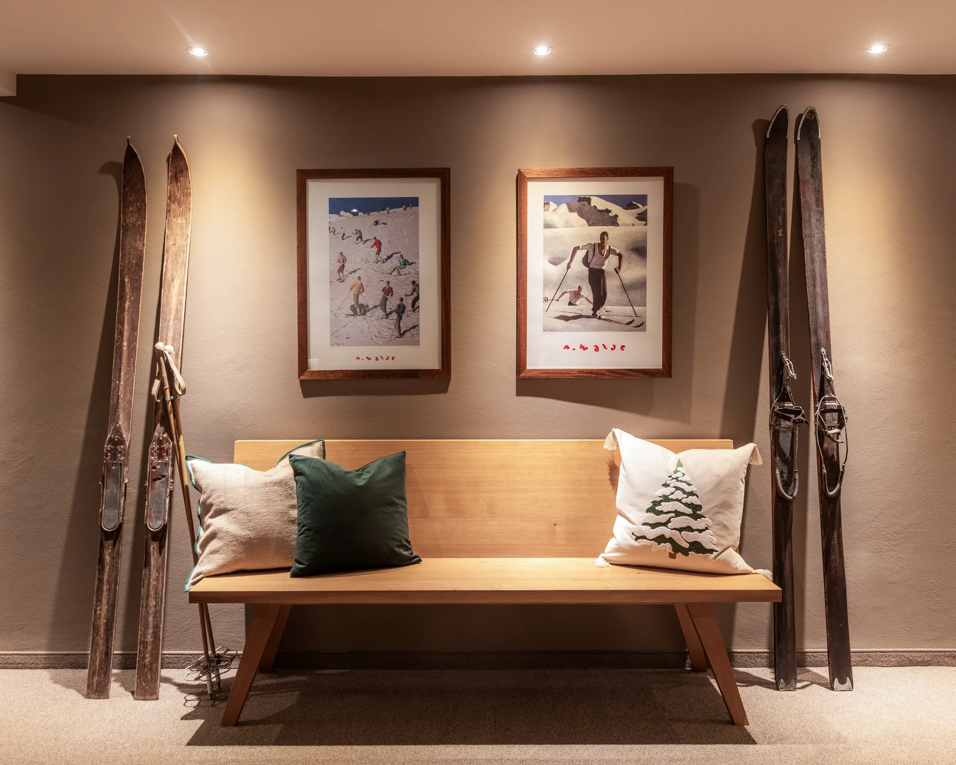 Holzbank mit Kissen unter zwei gerahmten Skifahrer-Bildern und antiken Skiern an der Wand