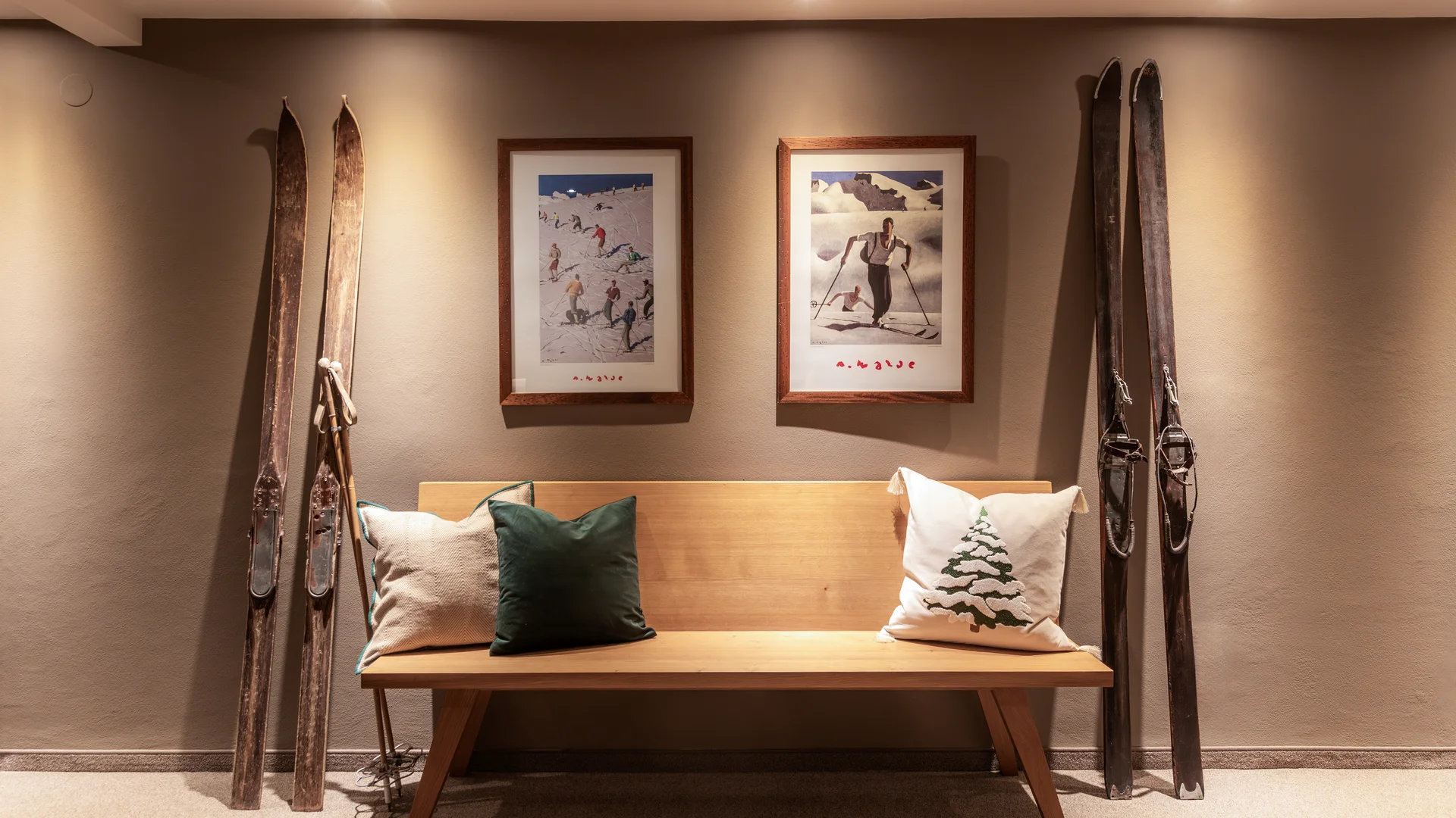 Holzbank mit Kissen unter zwei gerahmten Skifahrer-Bildern und antiken Skiern an der Wand