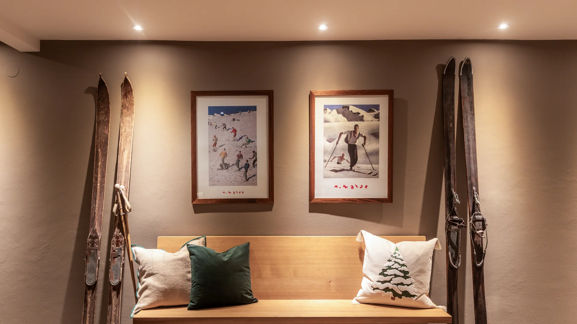 Holzbank mit Kissen unter zwei gerahmten Skifahrer-Bildern und antiken Skiern an der Wand