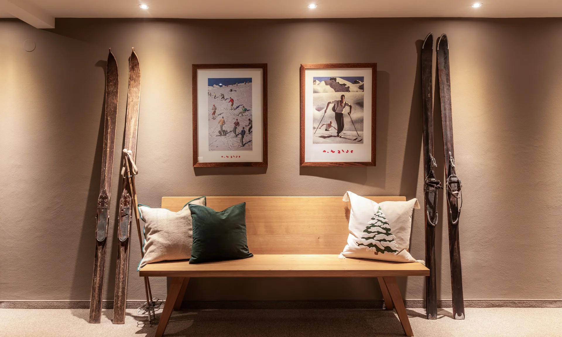 Holzbank mit Kissen unter zwei gerahmten Skifahrer-Bildern und antiken Skiern an der Wand