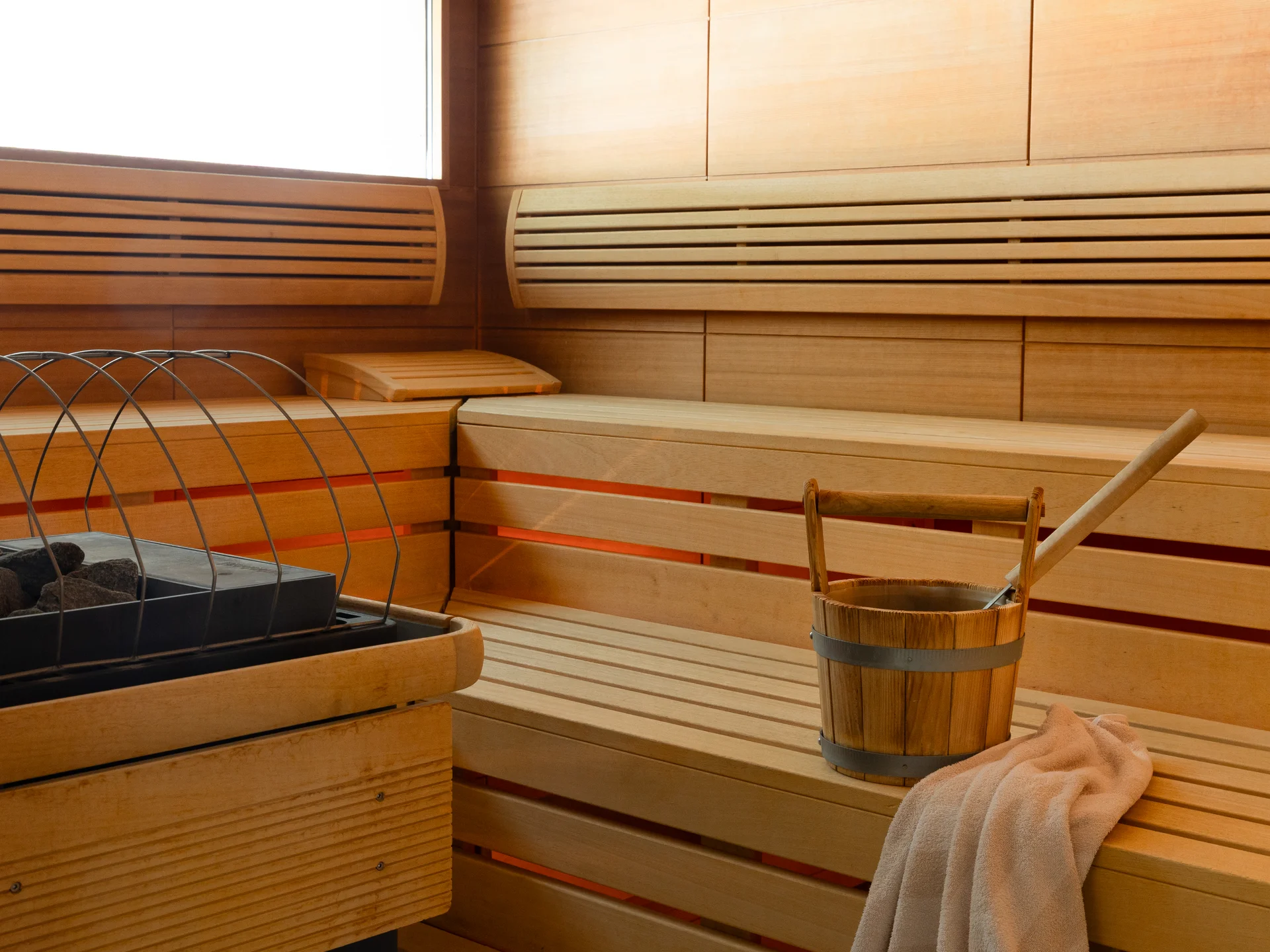 Innenraum einer Holzsauna mit Ofen, Holzeimer und Handtuch
