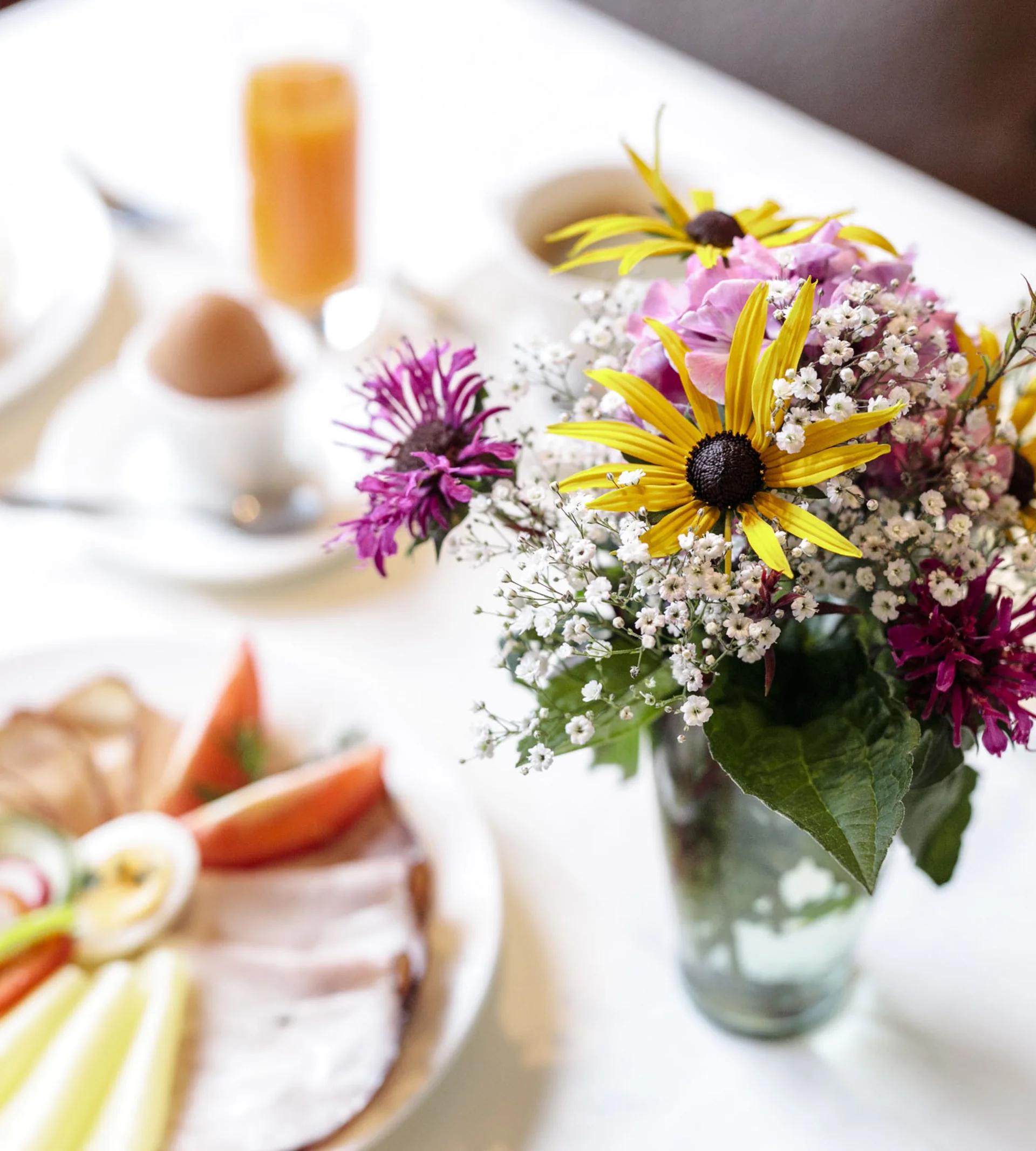 Bunter Blumenstrauß in Glasvase auf gedecktem Frühstückstisch