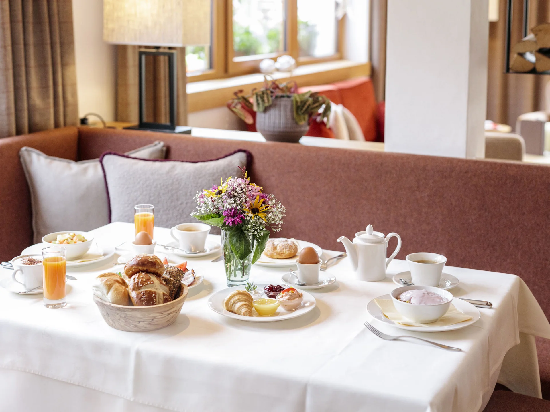 Frühstückstisch mit Brötchen, Eiern, Kaffee und Blumen in gemütlicher Atmosphäre