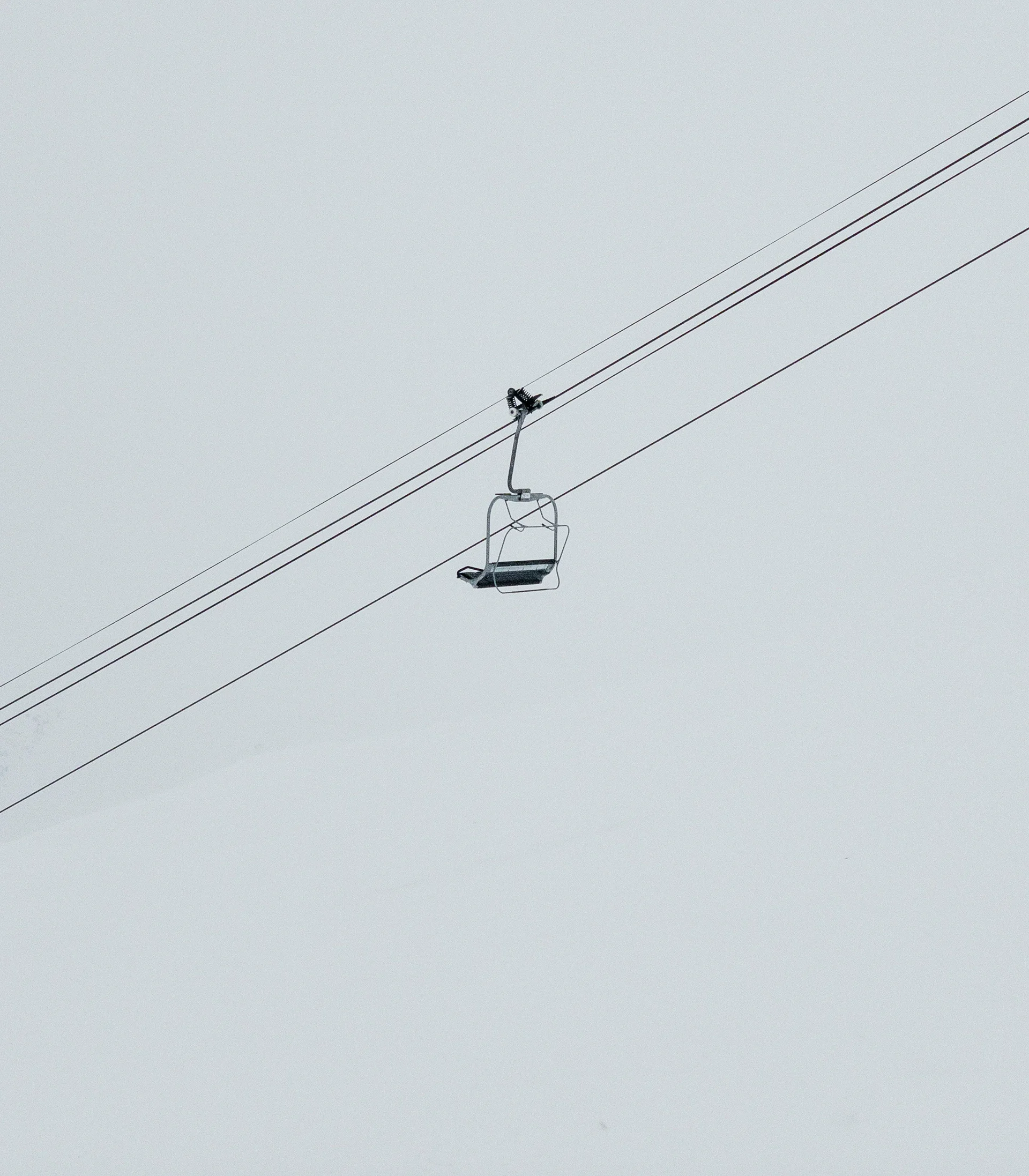 Leerer Skiliftstuhl vor nebligem Himmel und schneebedeckter Landschaft