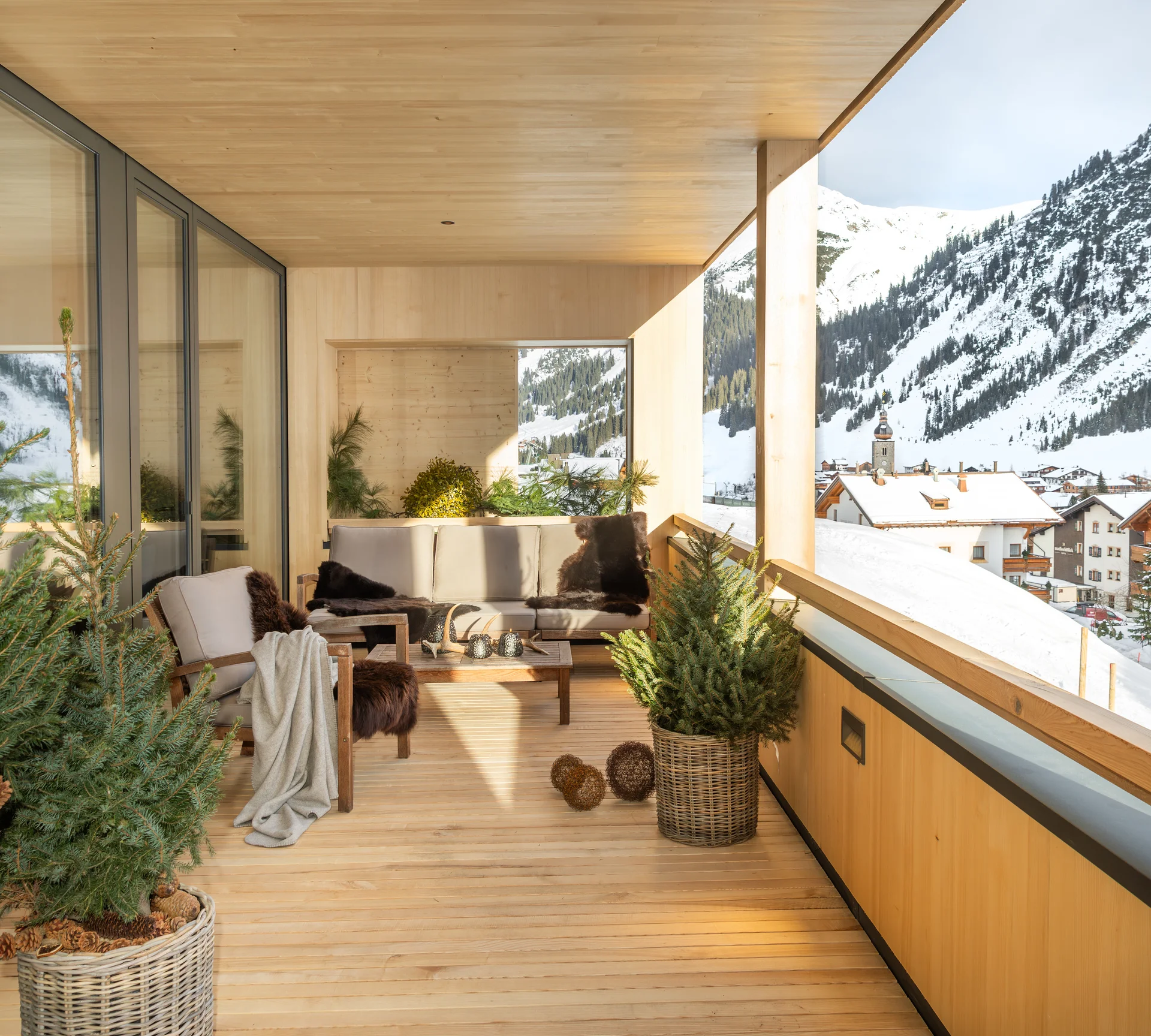Überdachter Holz-Balkon mit Sitzmöbeln und Blick auf verschneite Berge und Dorf