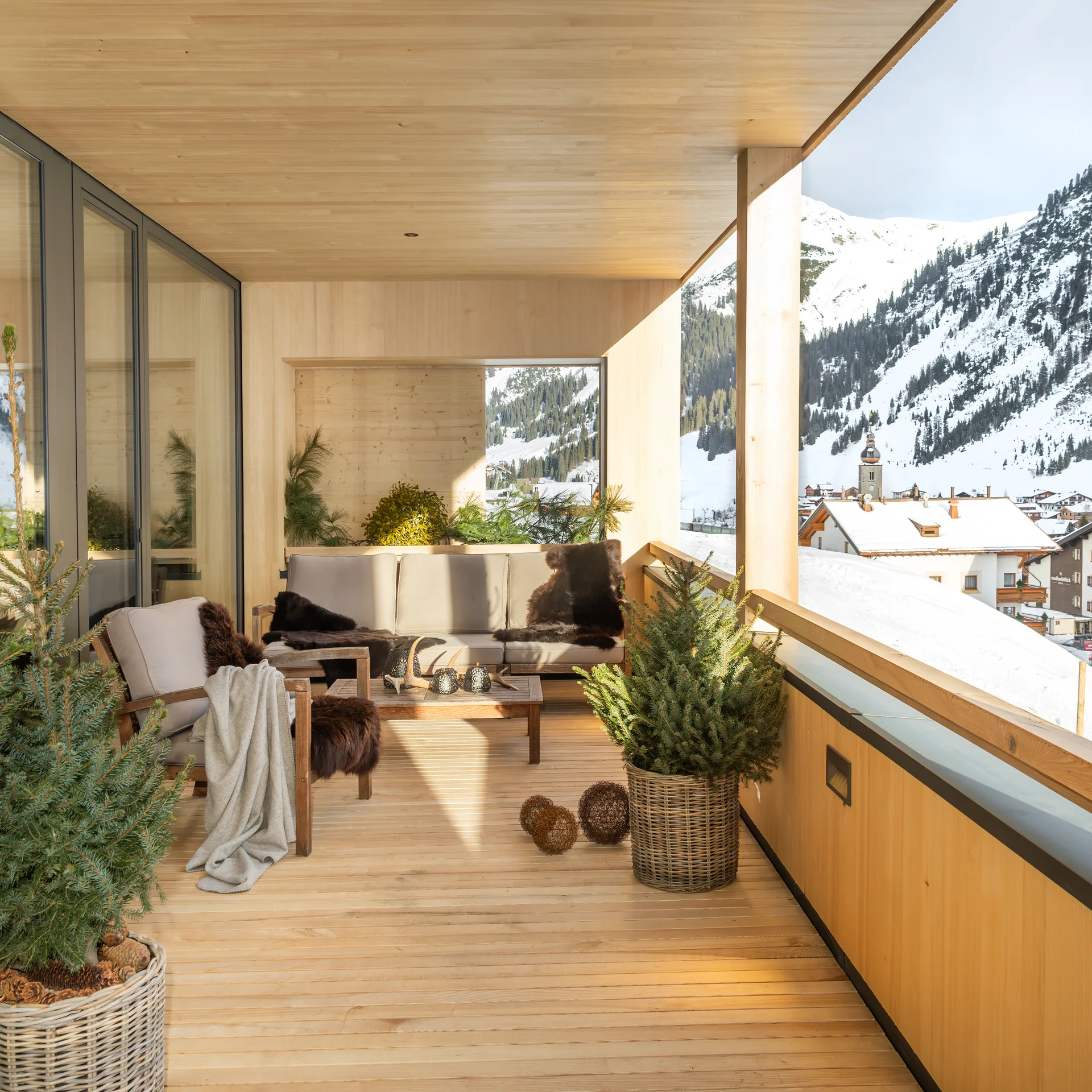 Überdachter Holz-Balkon mit Sitzmöbeln und Blick auf verschneite Berge und Dorf