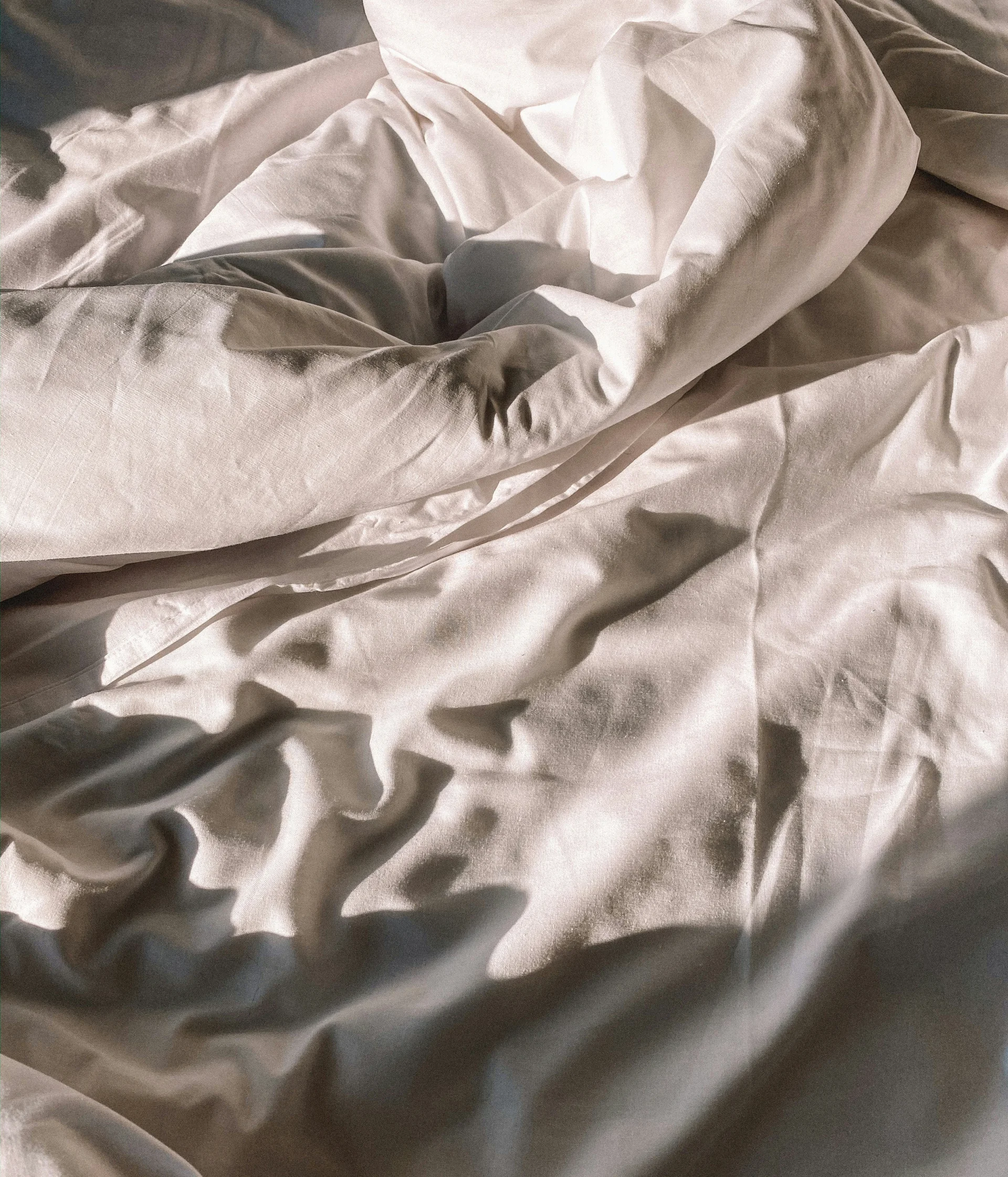 Weißes zerknittertes Bettlaken mit Sonnenlicht und Schatten