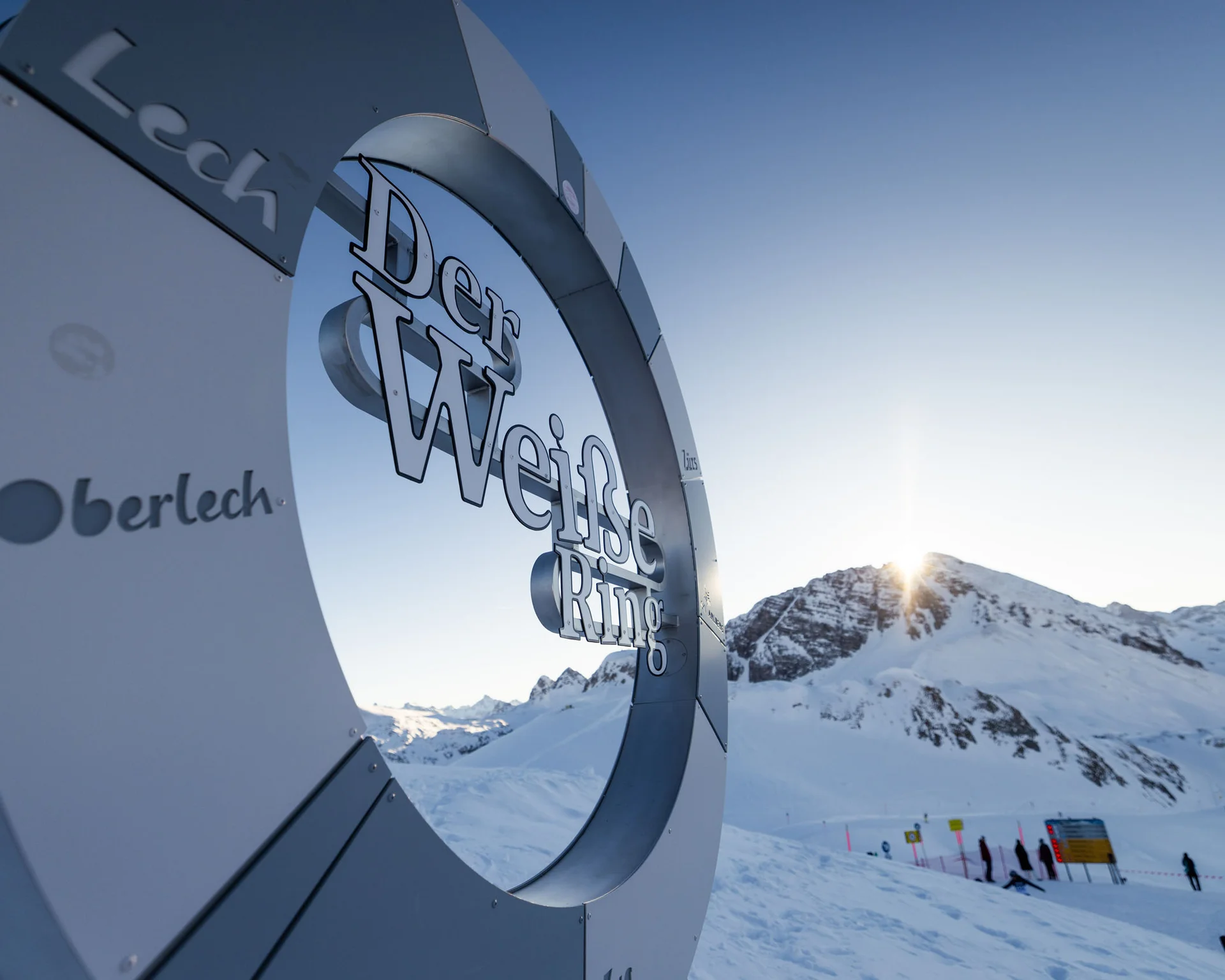 Metallskulptur der Weißen Ring Skiroute vor schneebedeckten Bergen bei Sonnenuntergang