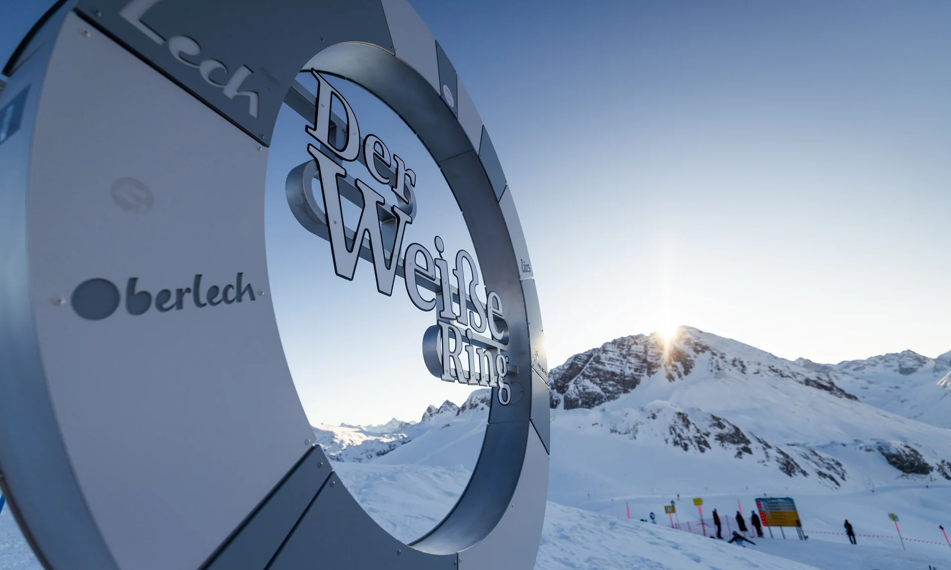 Metallskulptur der Weißen Ring Skiroute vor schneebedeckten Bergen bei Sonnenuntergang