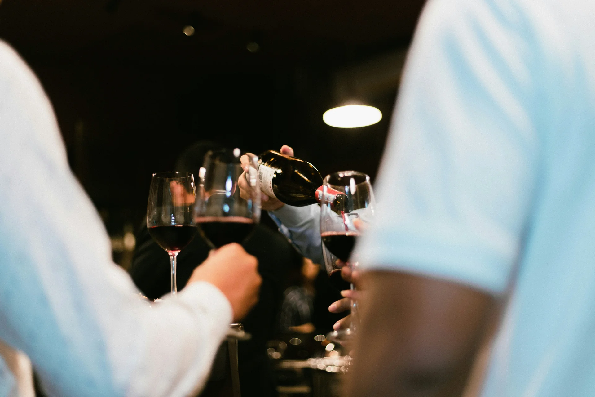 Person gießt Rotwein in Gläser bei einer gesellschaftlichen Zusammenkunft