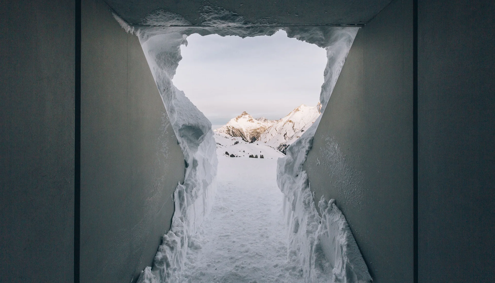 Blick durch ein schneebedecktes Fenster auf verschneite Berge