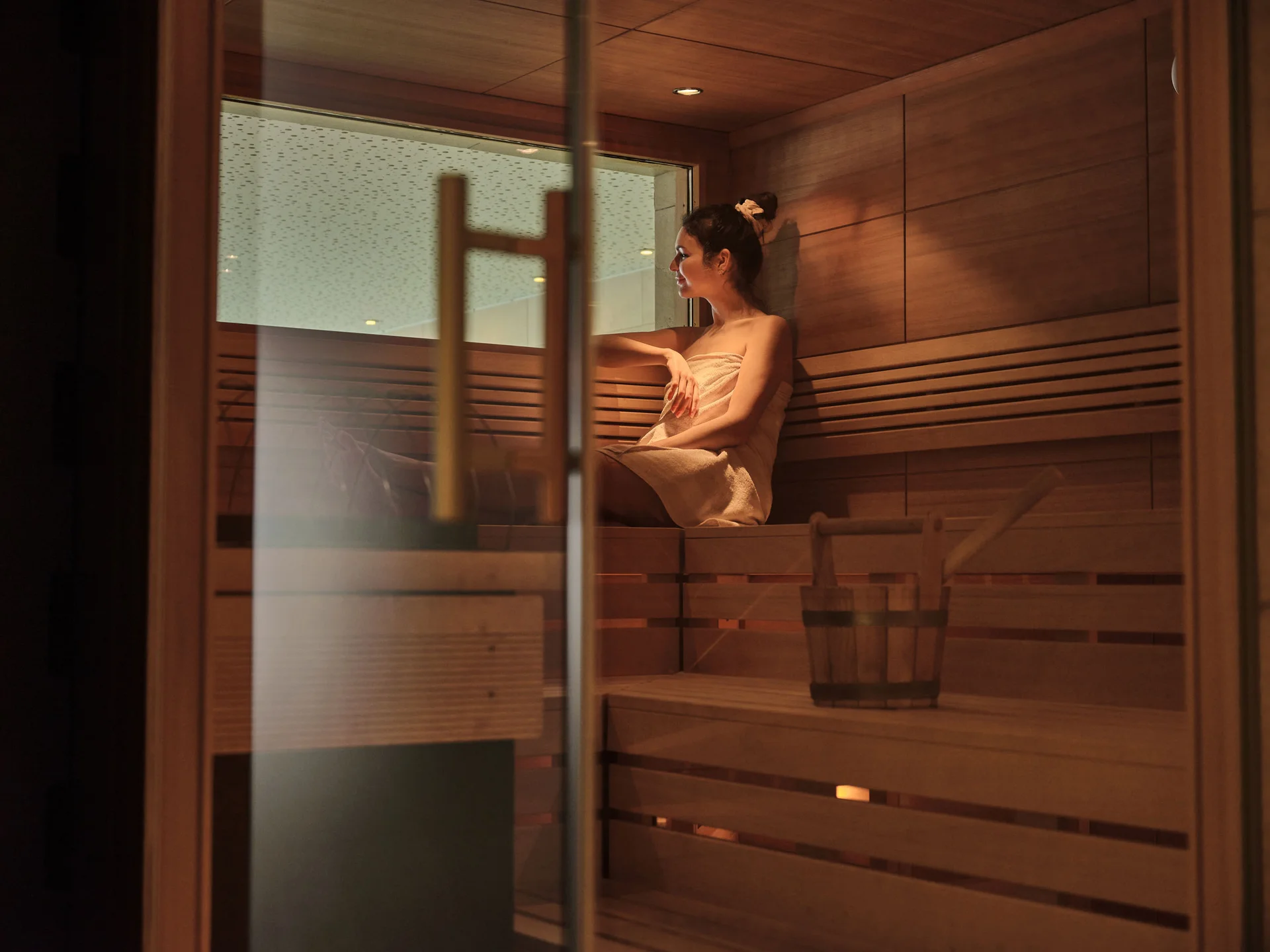 Frau entspannt in Sauna, sitzt auf Holzbank mit Handtuch